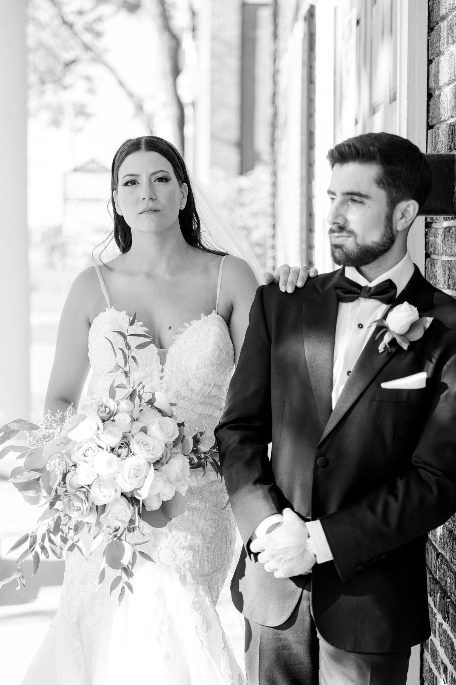 A classic black and white wedding portrait of a couple posed against a brick wall.