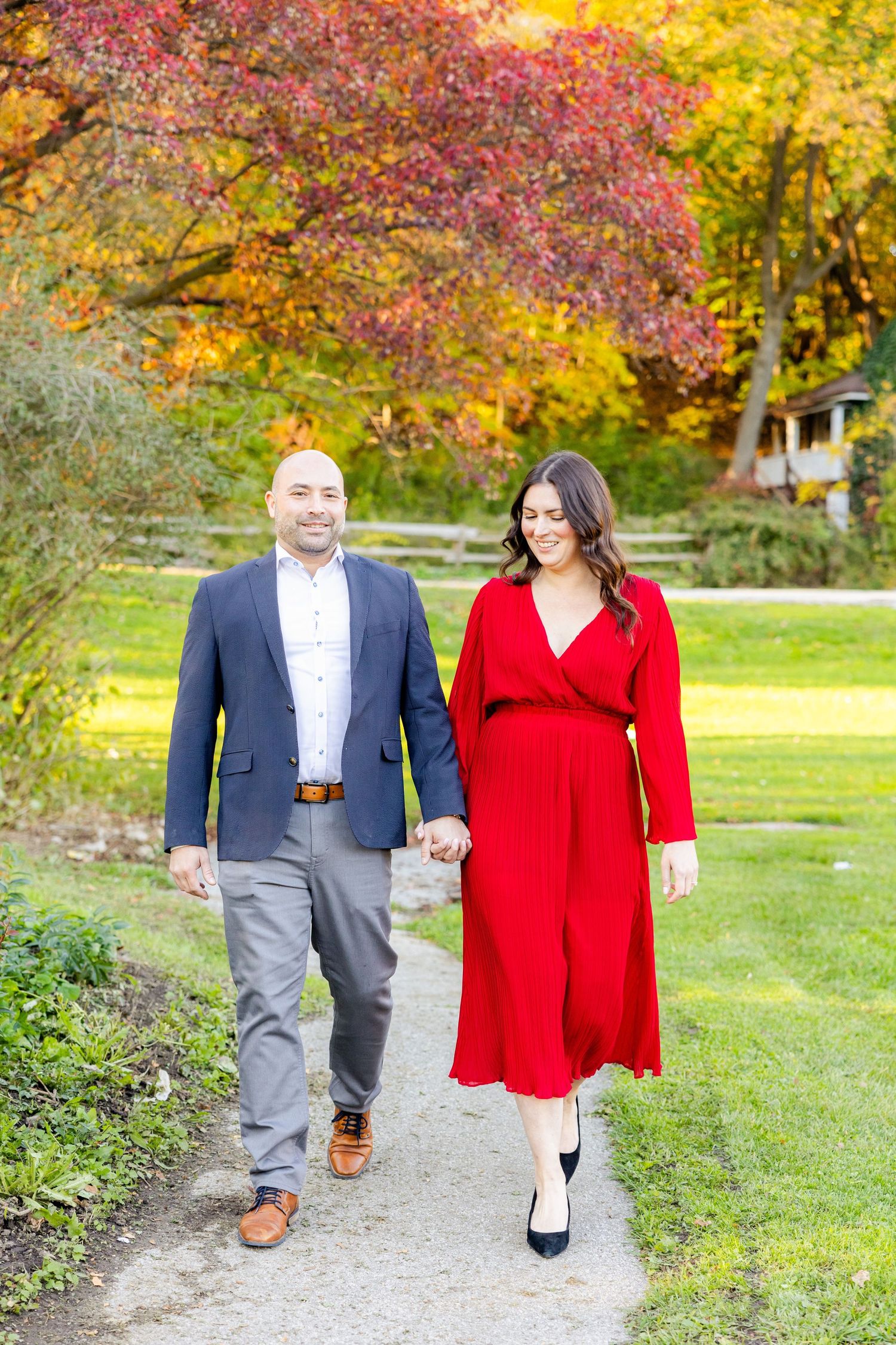 A couple takes a romantic autumn stroll along a garden path with red and yellow foliage above.