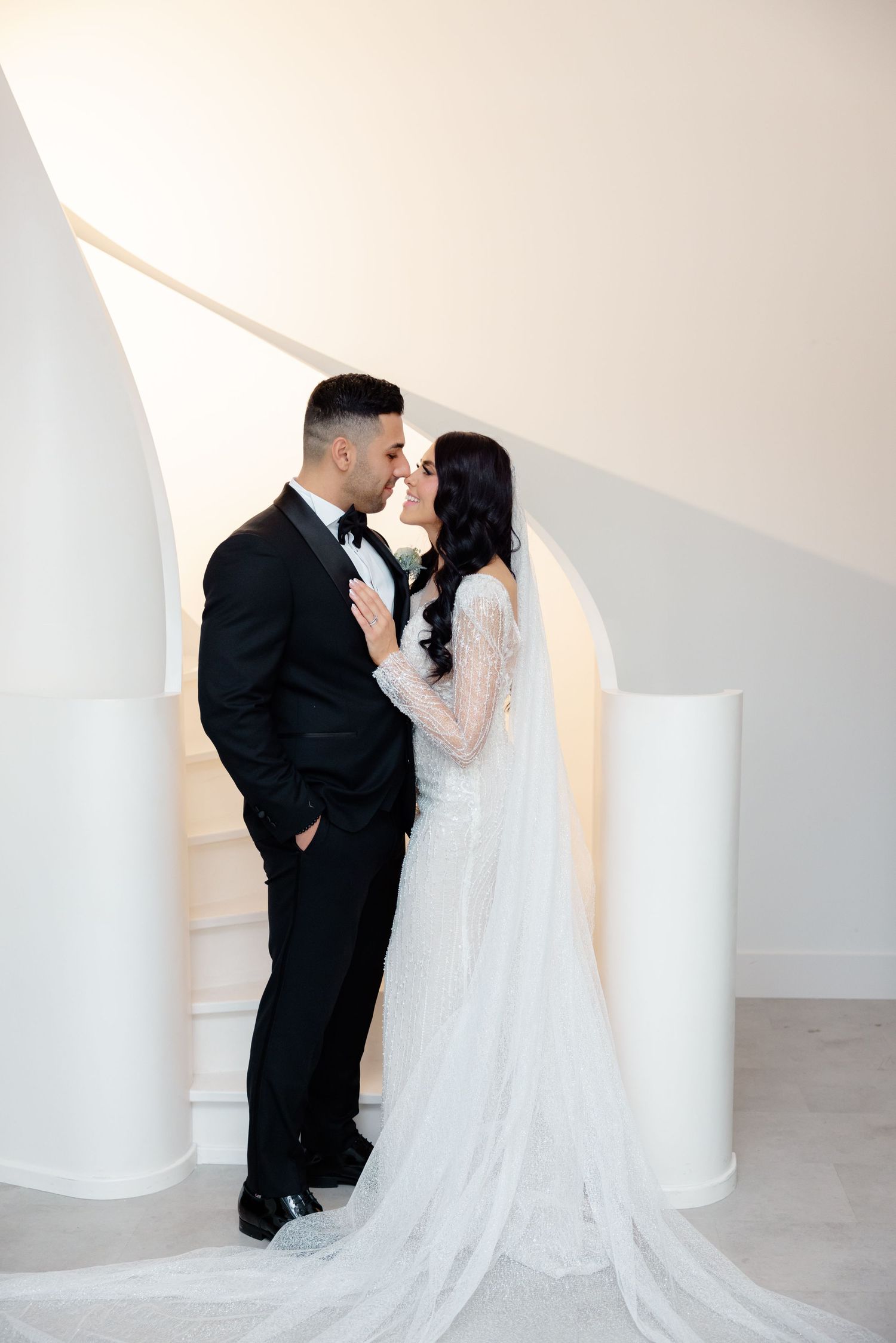 Intimate wedding portrait captured against minimalist white architectural backdrop.
