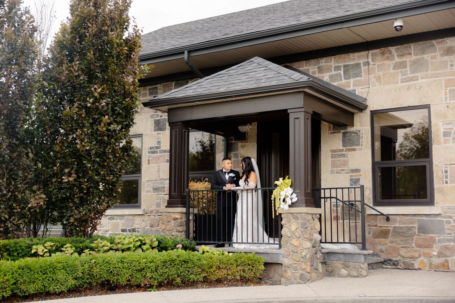 Modern stone ranch home exterior showcases covered entryway with white railings and black metal columns.