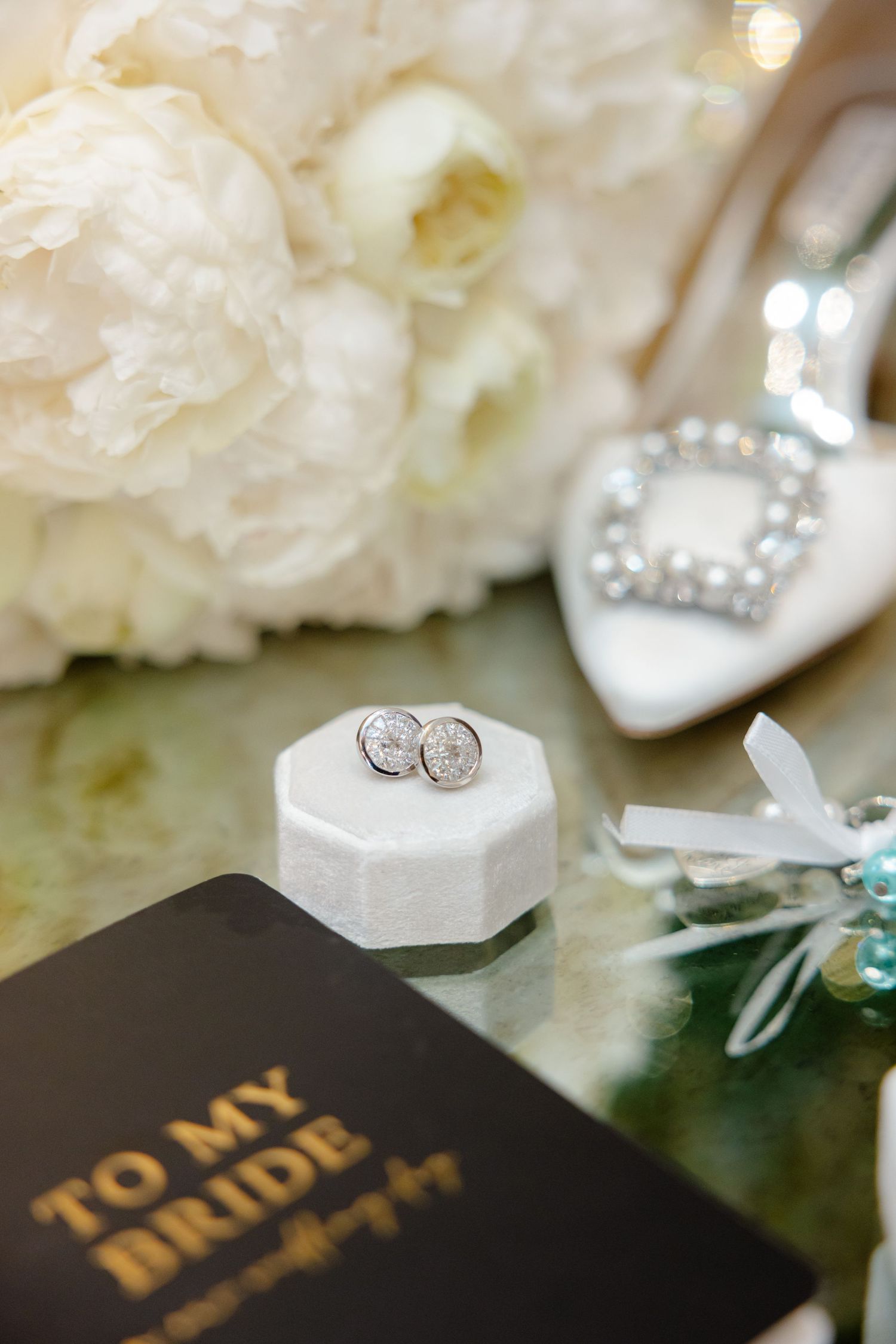 Wedding rings in white octagonal box next to 'To My Bride' book and white floral decor.
