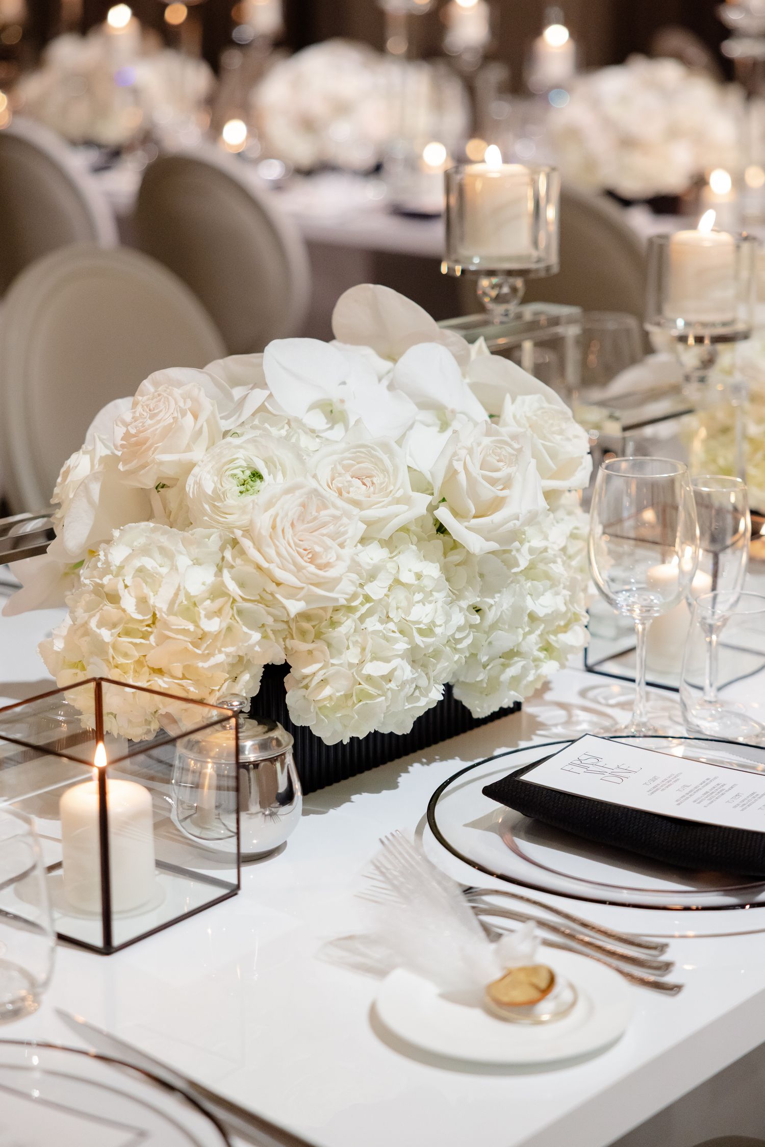 Elegant wedding table setting with white hydrangeas and roses centerpiece, glowing candles and crystal glassware.