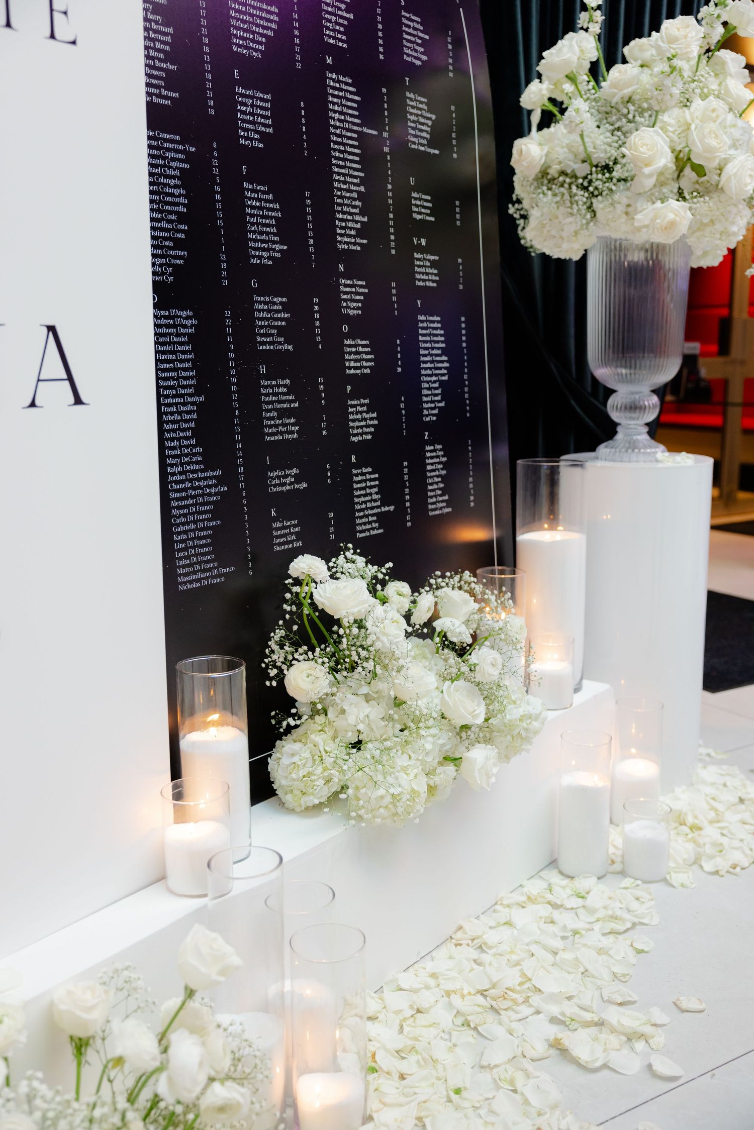 Seating chart display decorated with white flowers and glowing candles.