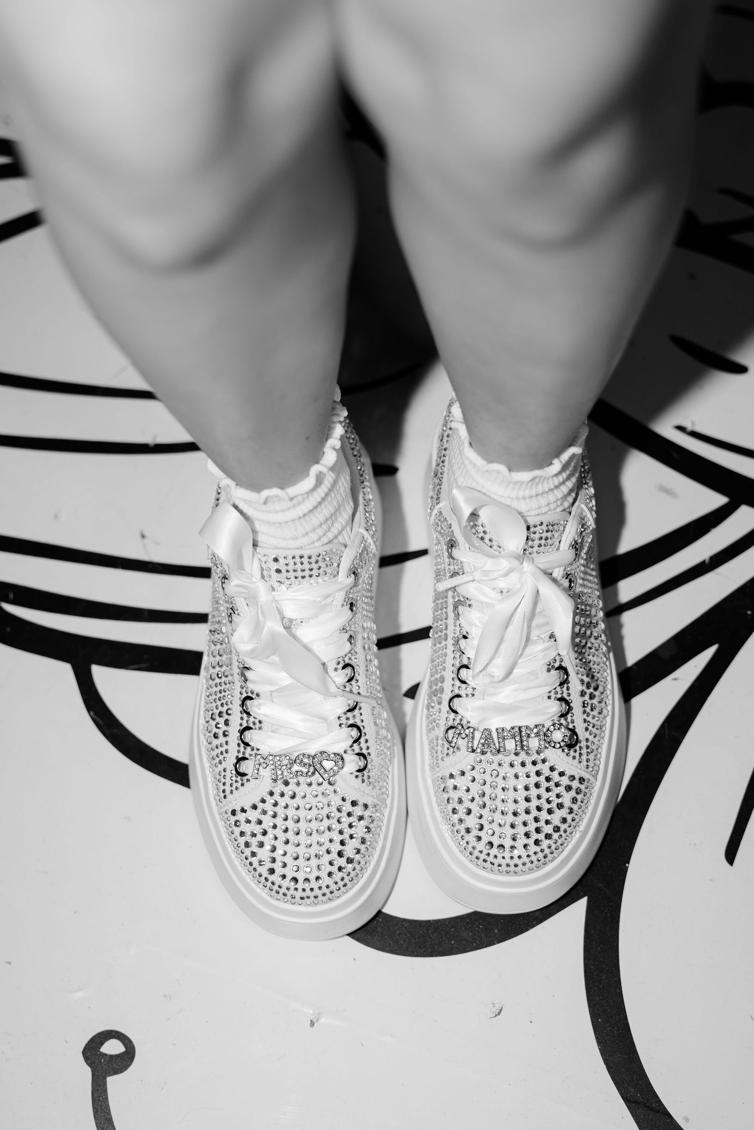 Crystal-embellished white sneakers with rhinestone details on a black and white patterned floor.