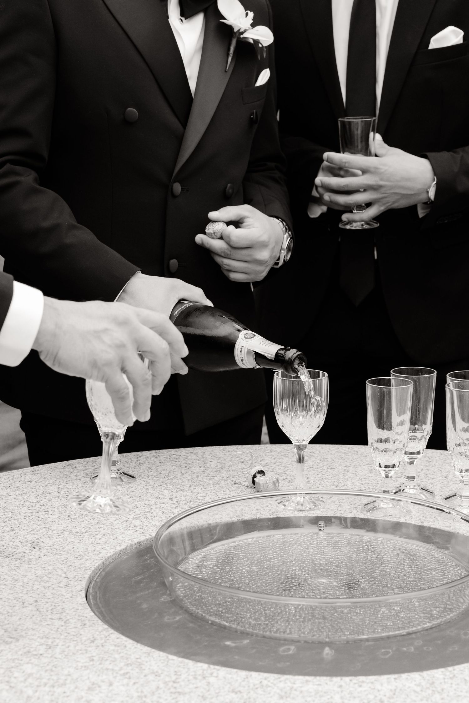 Black and white photo series showing hands in formal attire performing a champagne pouring sequence at an elegant event.