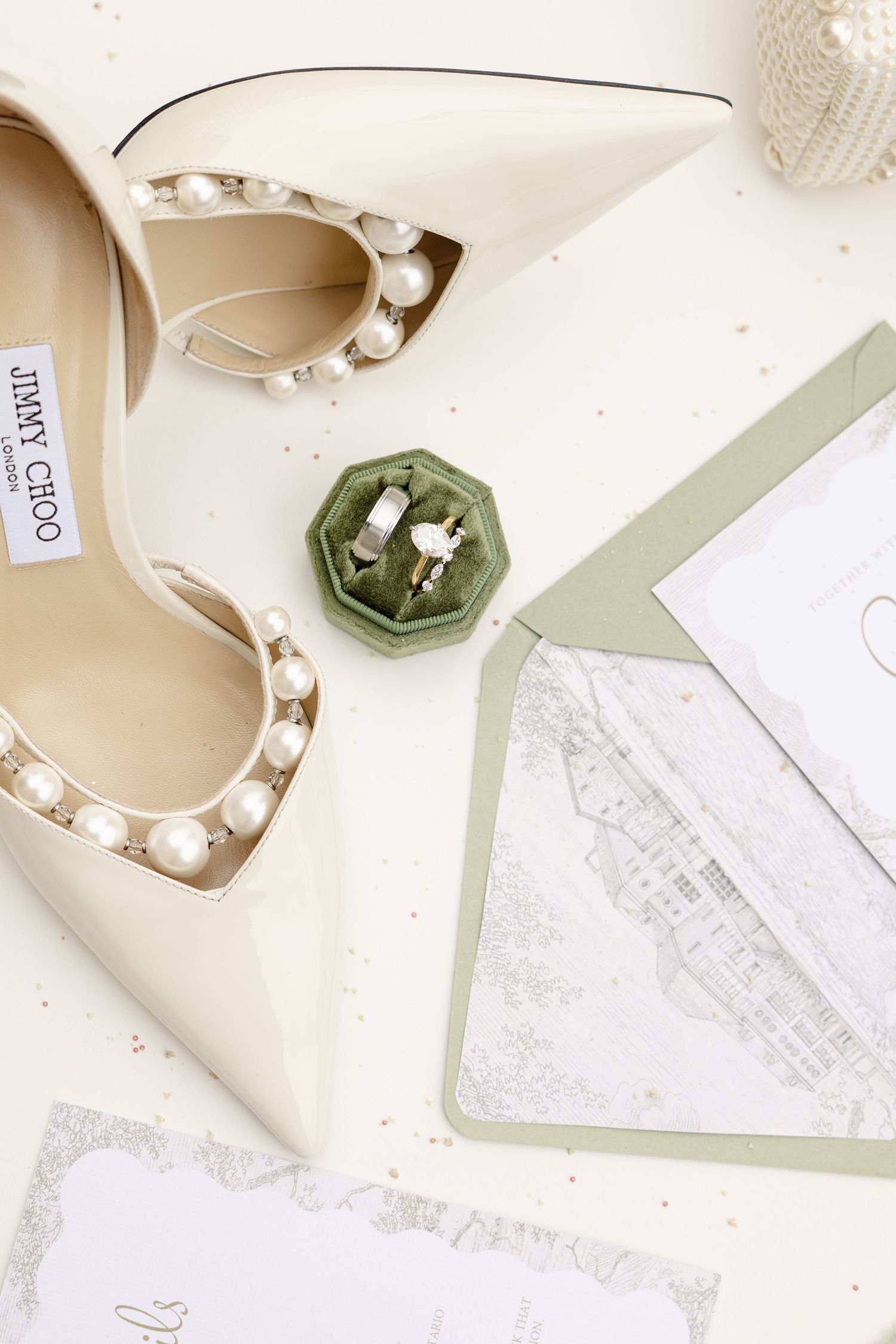Pearl and diamond engagement rings displayed on a green velvet hexagonal ring holder with floral backdrop.