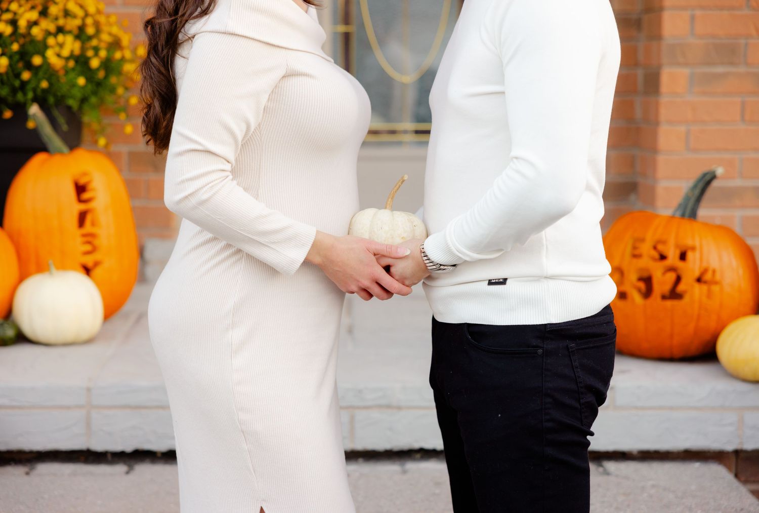 Couple holding hands in front of pumpkin display, suggesting autumn pregnancy announcement.