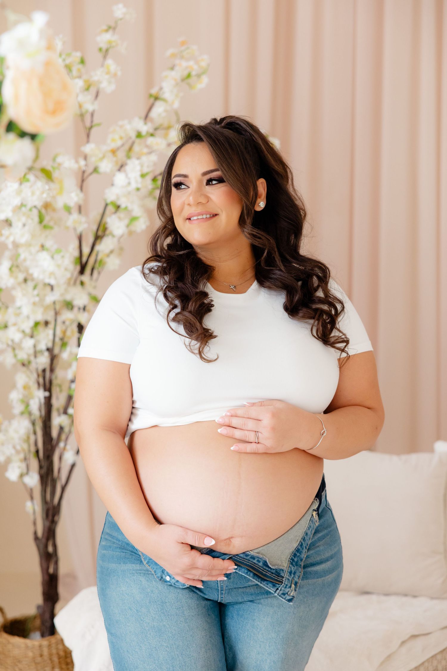 A pregnant woman in a white t-shirt and jeans poses against a floral backdrop for a maternity photo.