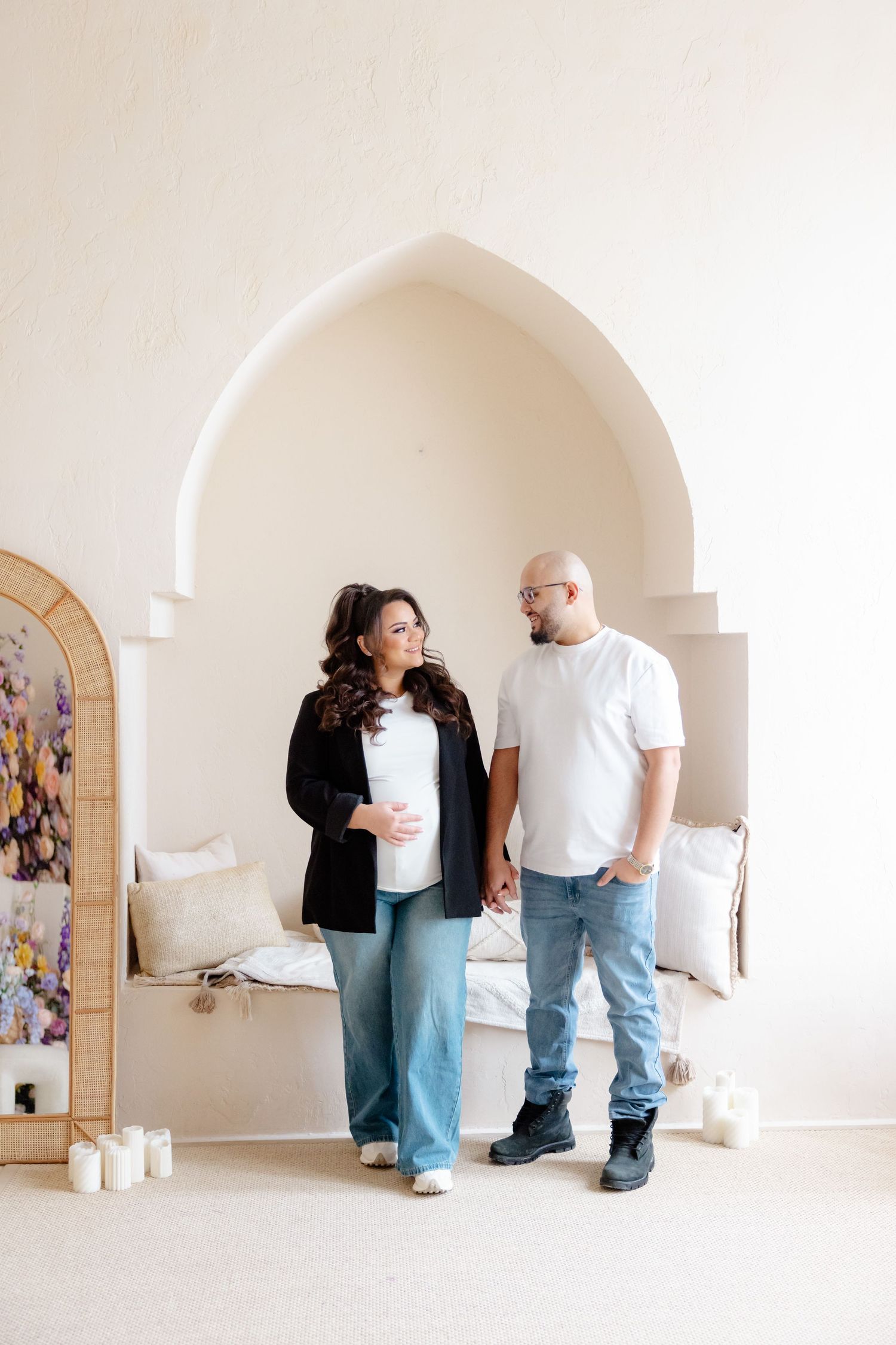 A couple stands lovingly in a bright white archway room with candles and decorative accents.