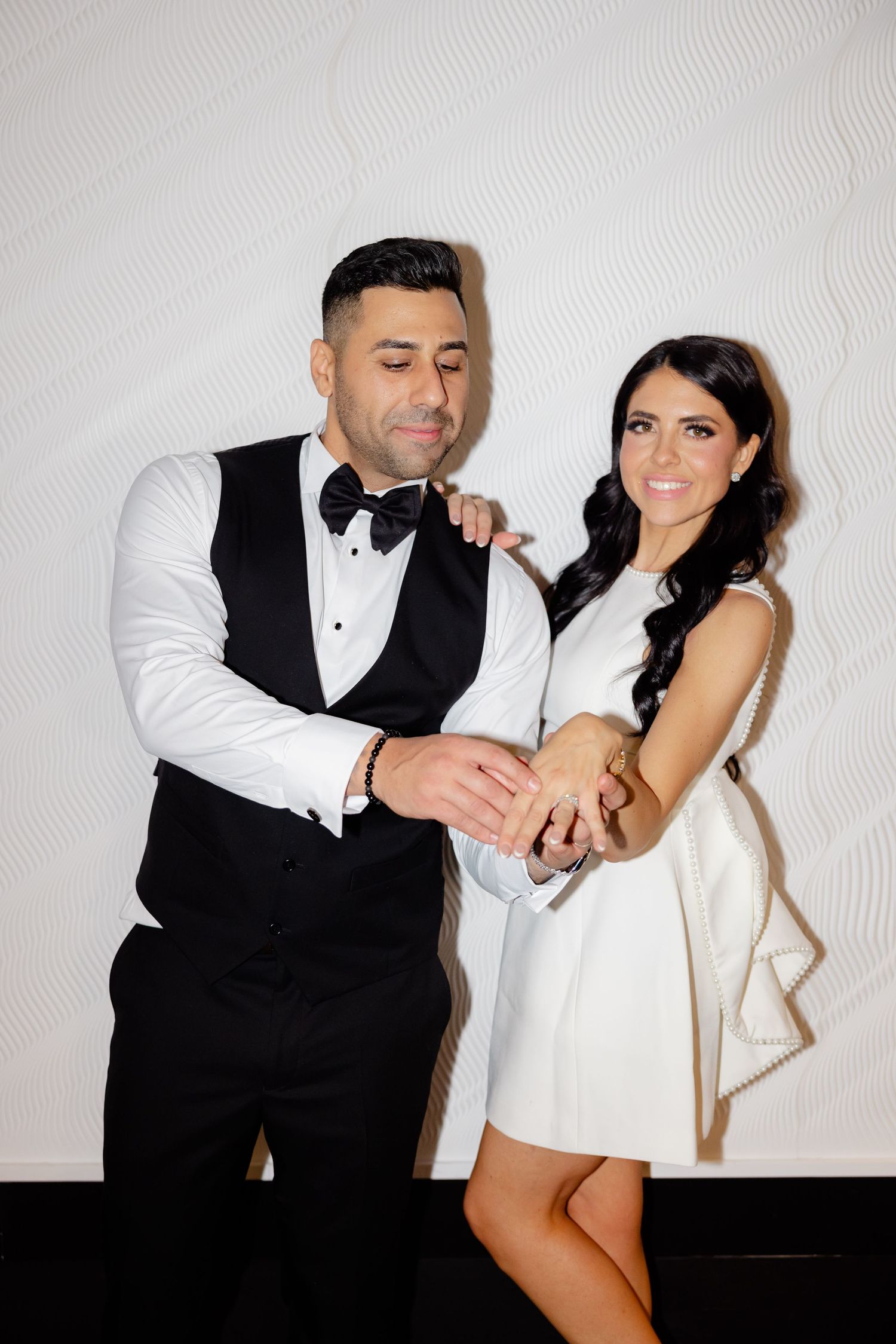 Couple in formal attire share intimate moment against white backdrop.