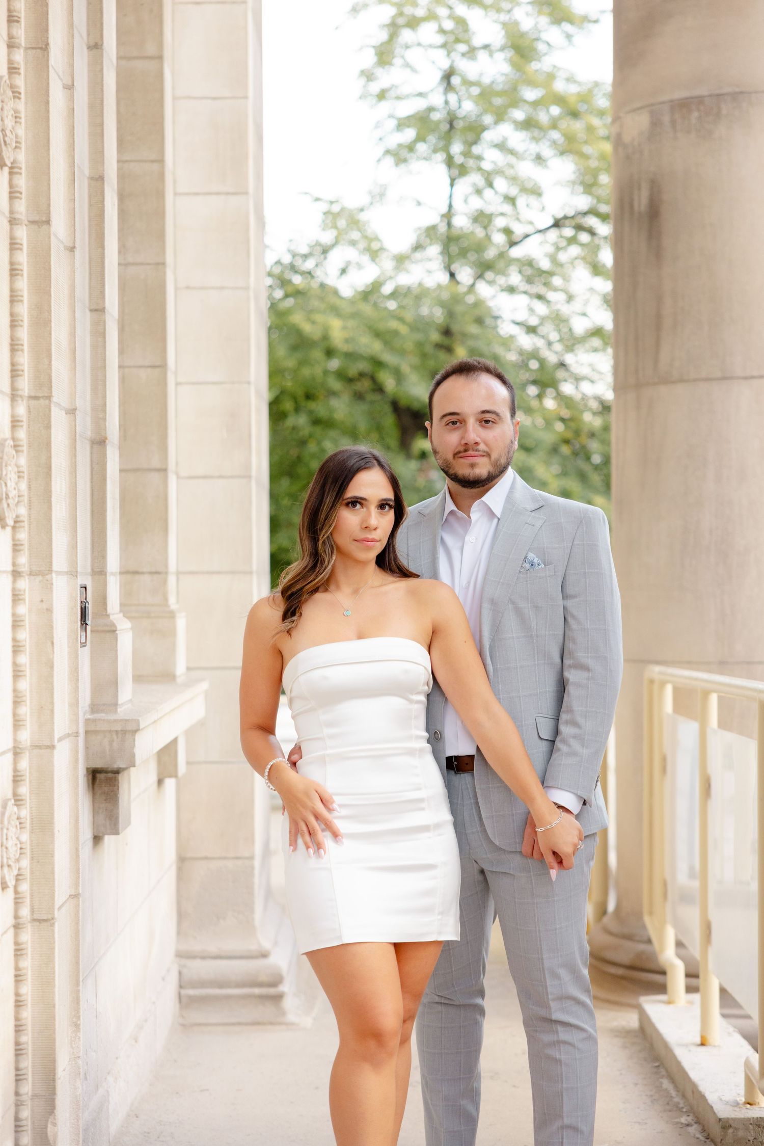 A romantic portrait of a couple standing between classical stone columns in formal attire.