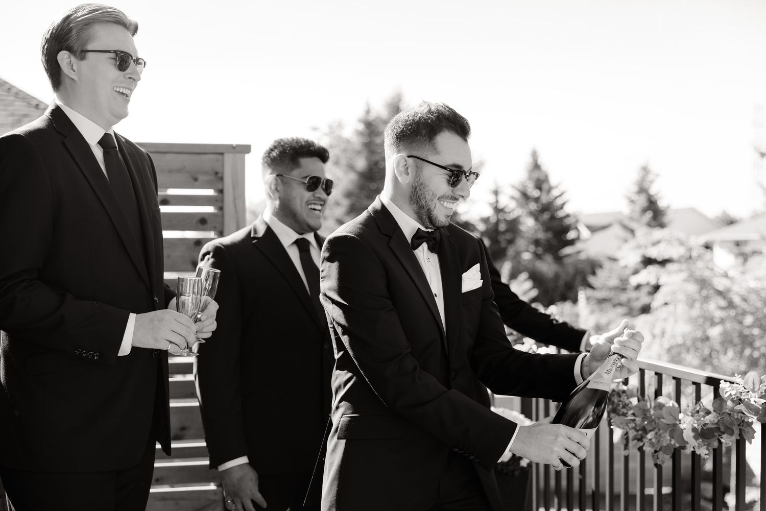 Three groomsmen in black tuxedos stand together in black and white photograph.