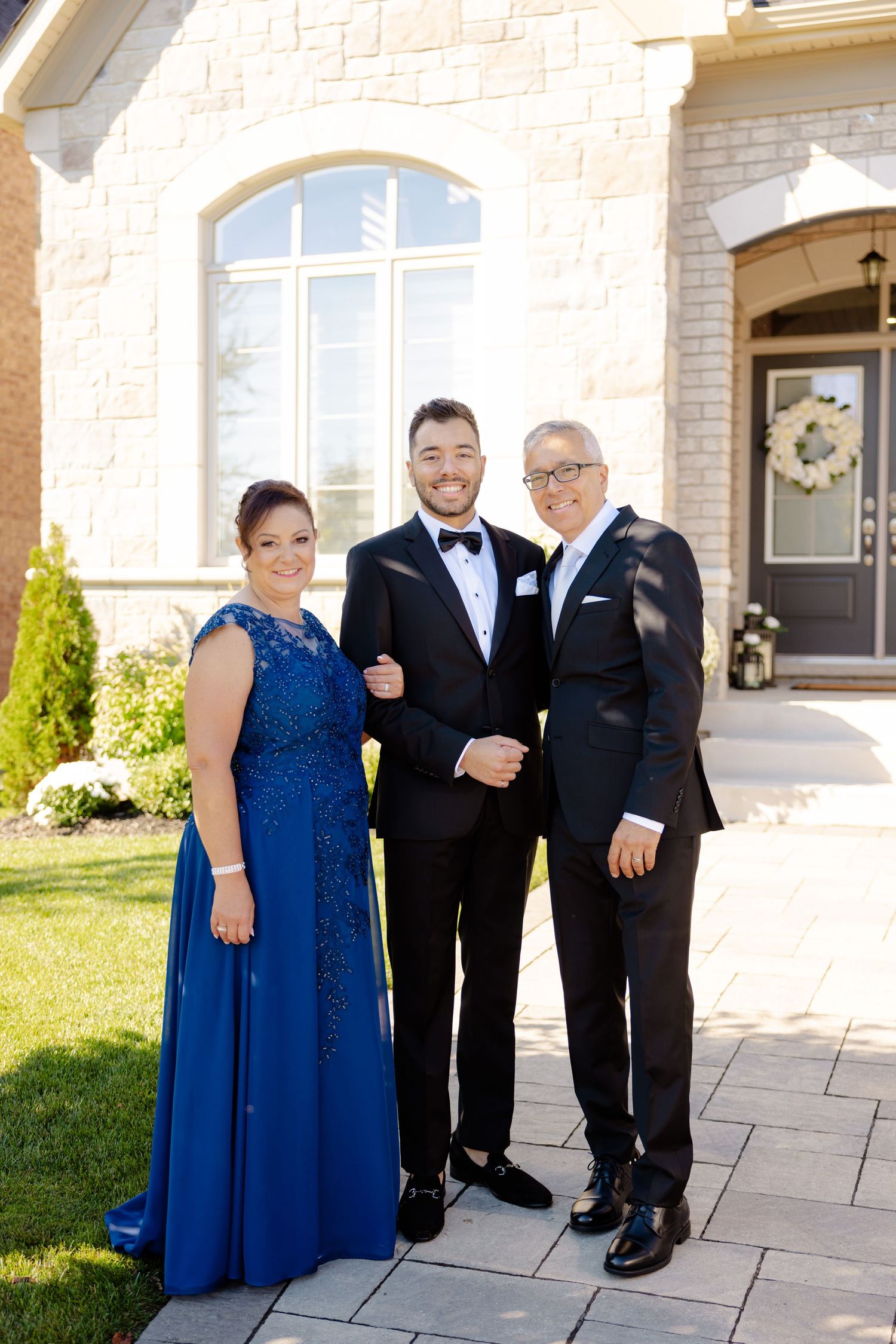 Wedding portrait of three people in formal attire outside stone church building.