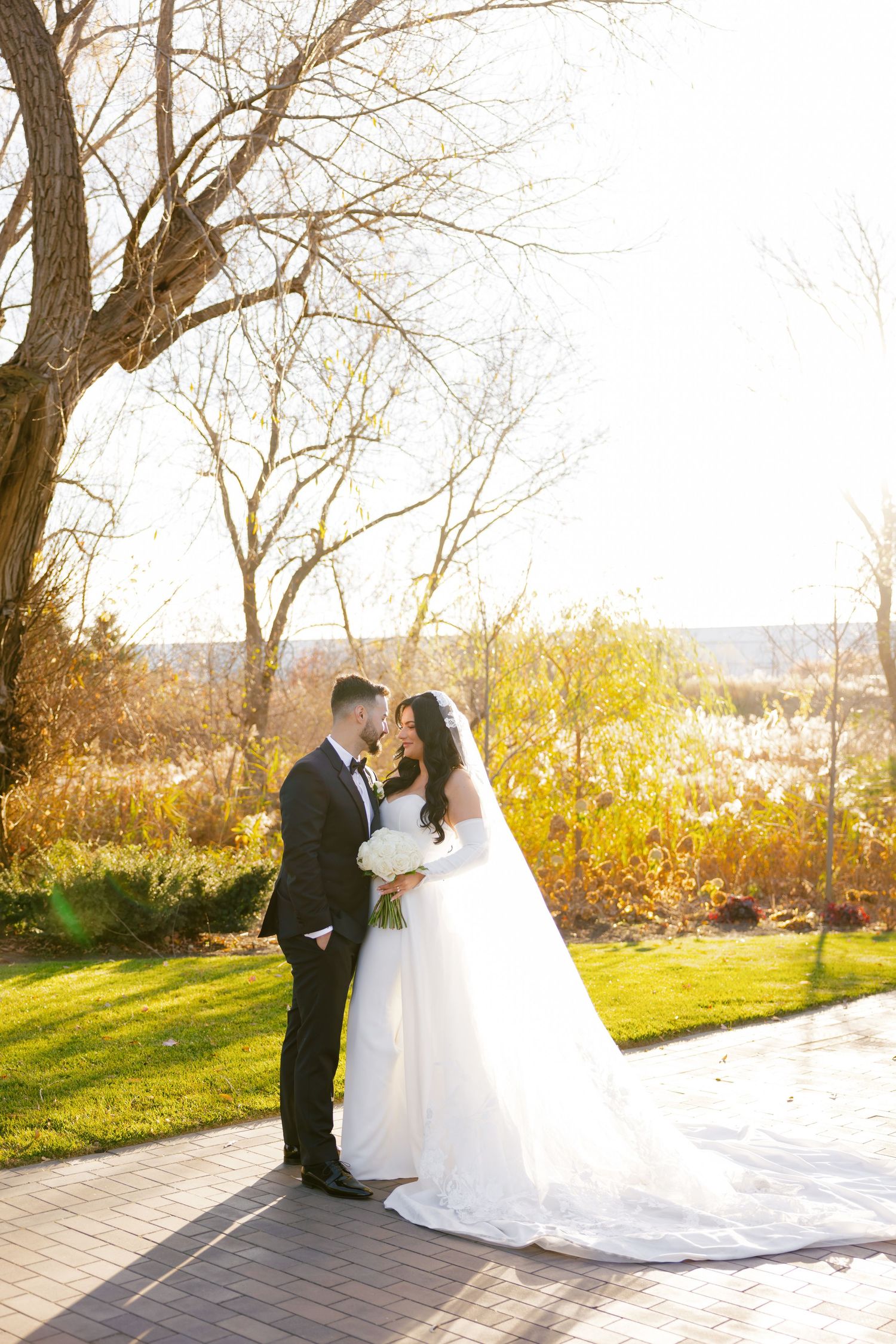 Newlyweds share an intimate moment on a garden path with glowing fall foliage behind them.