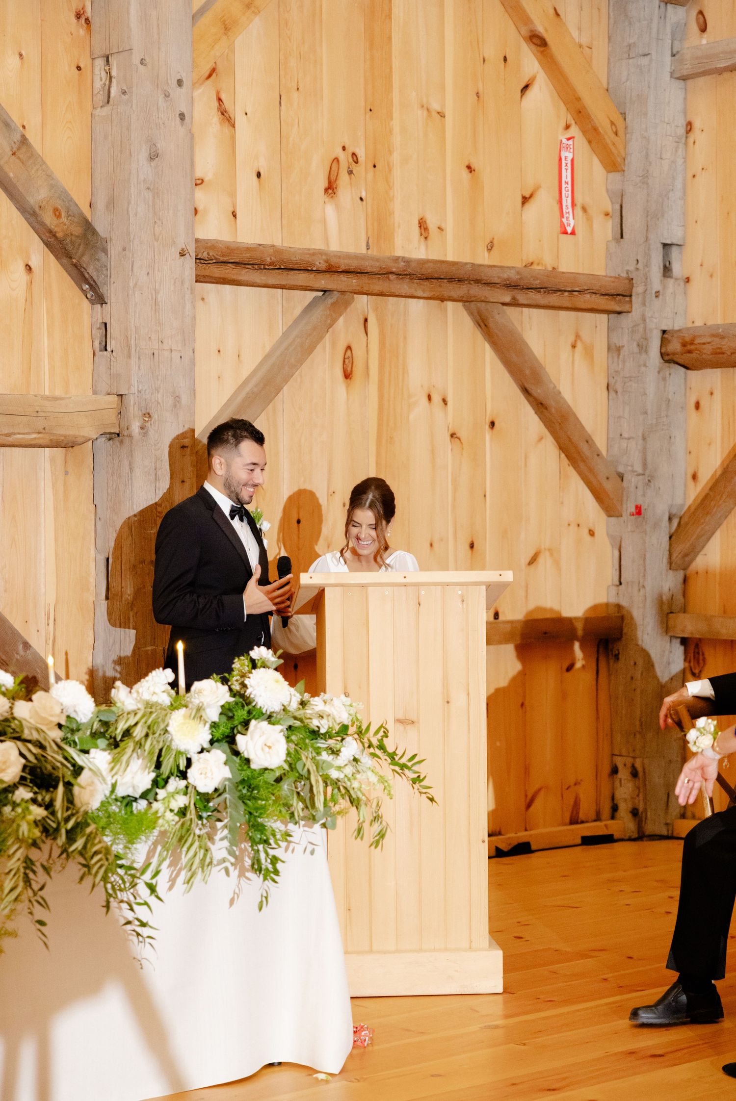 A wedding ceremony taking place in a rustic wooden barn with floral decor.