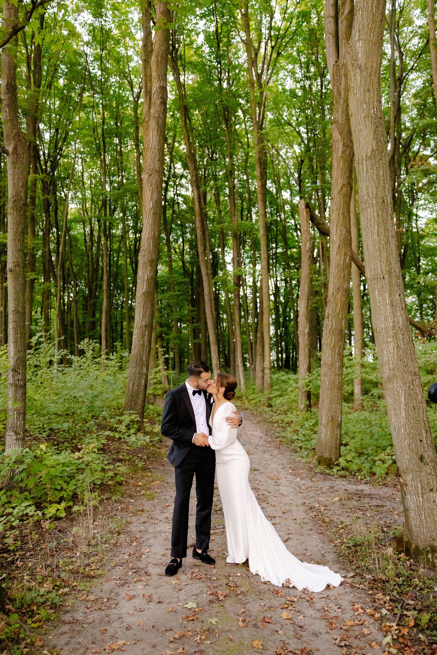 A tender moment between newlyweds on a wooded path with green foliage surrounding them.