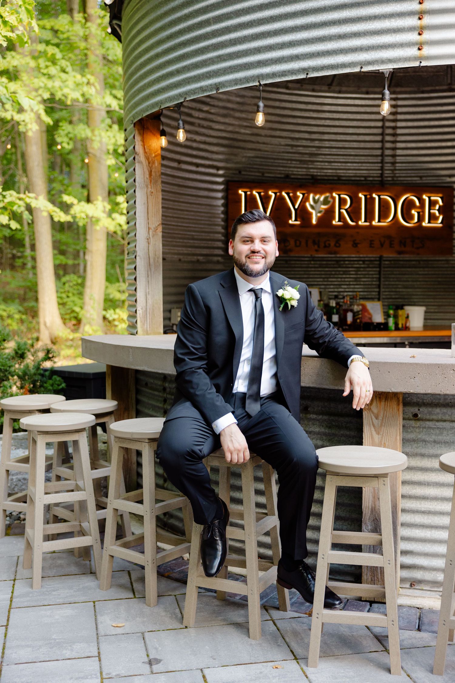 Formal portrait at rustic outdoor bar with illuminated Ivy Ridge sign.