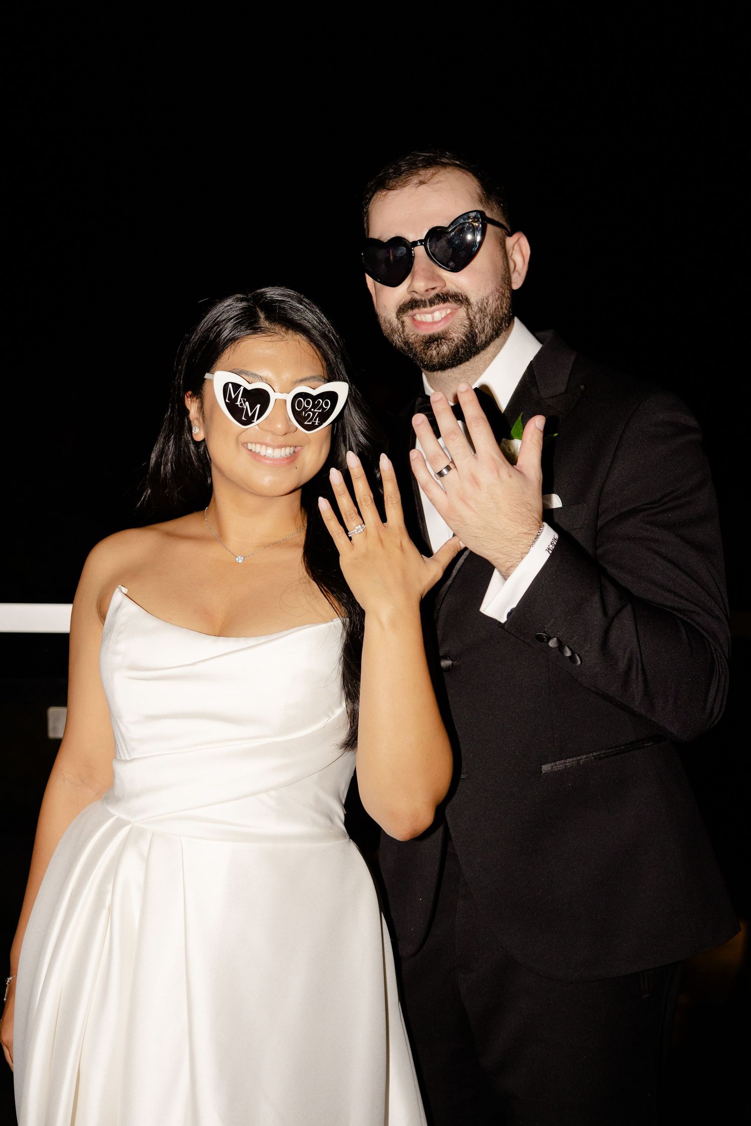 Wedding couple in matching heart sunglasses showing off their rings.