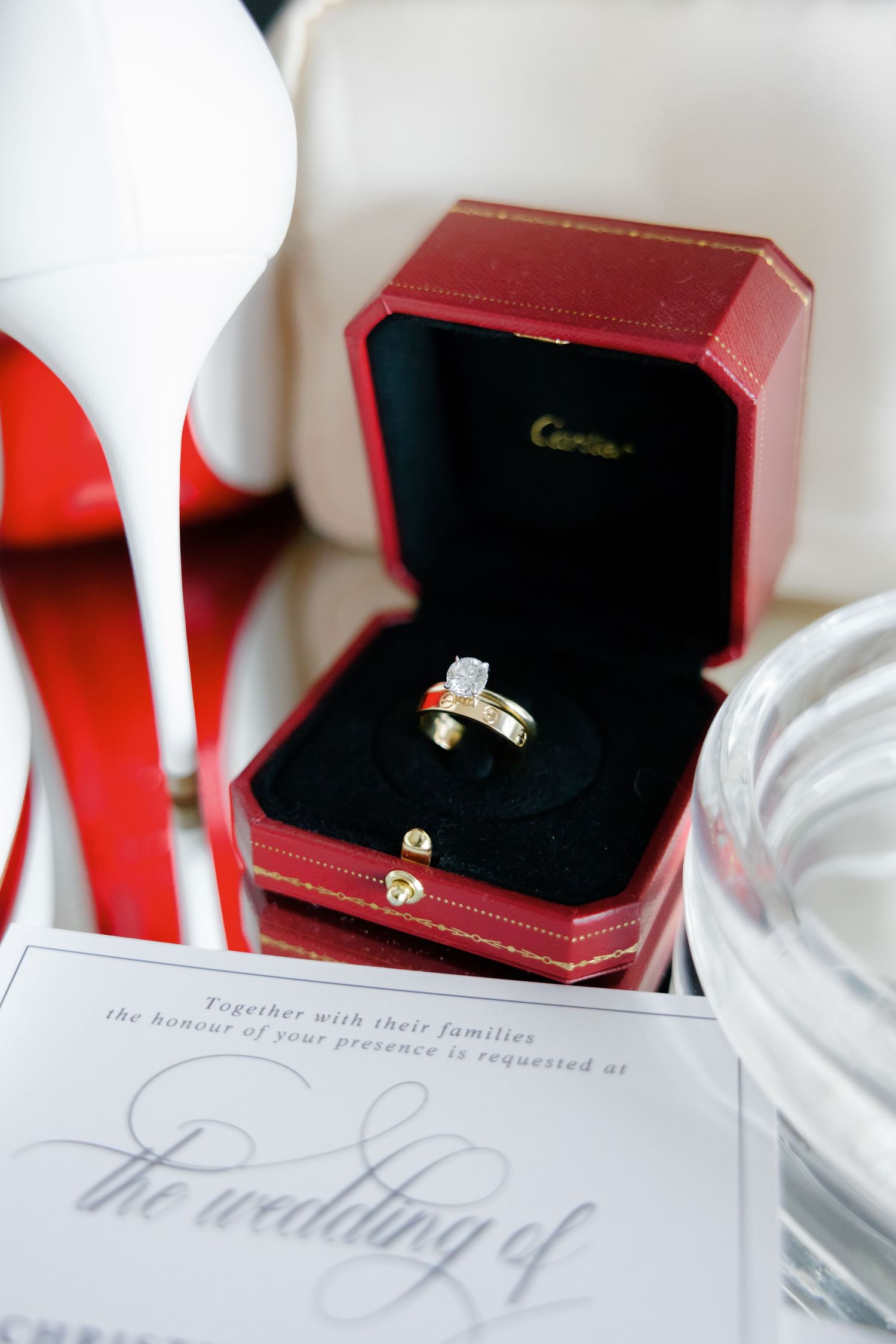 Diamond ring in red Cartier box with wedding invitation and white stiletto heel.