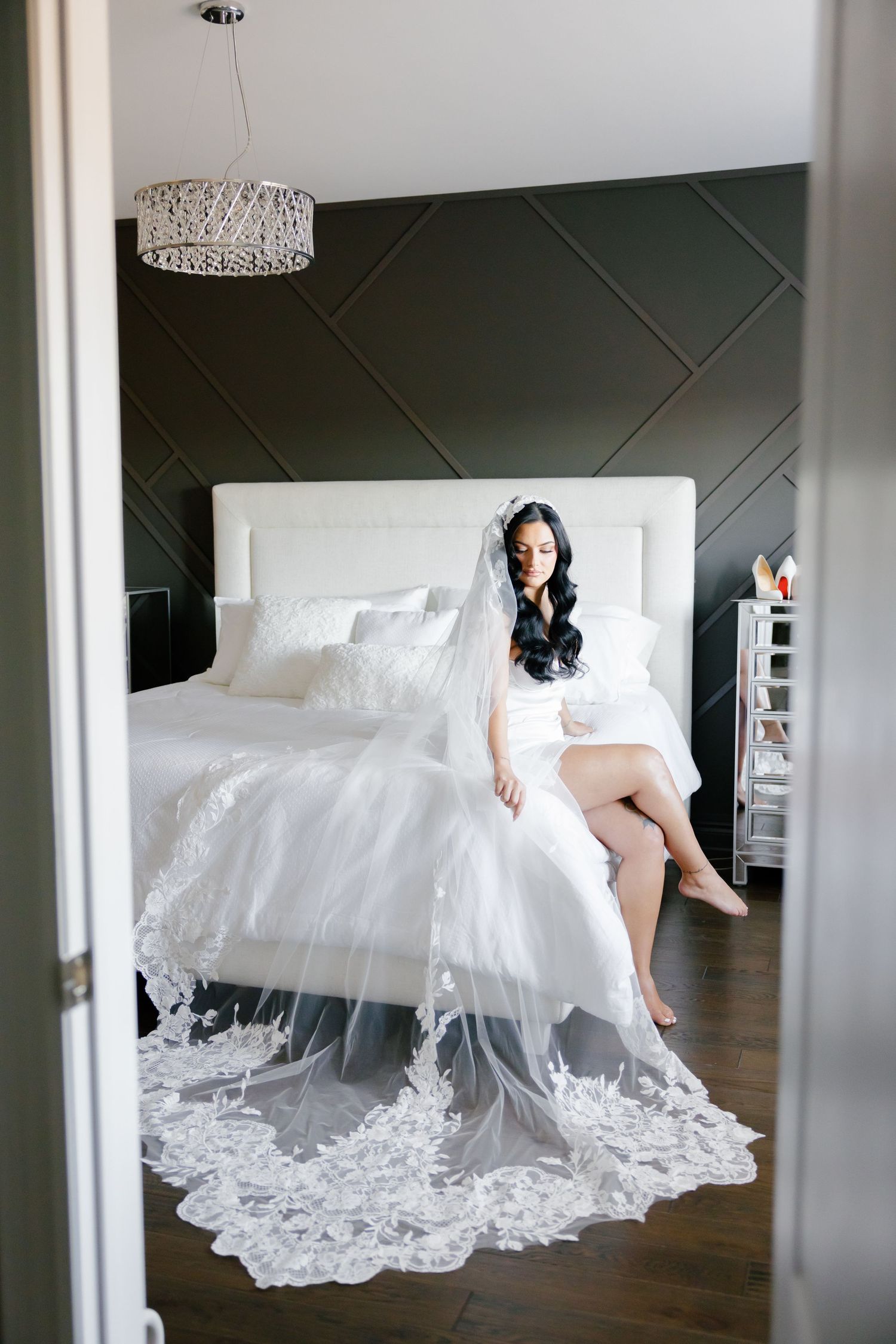 Elegant bridal portrait through doorframe featuring white bedding and geometric wall design.