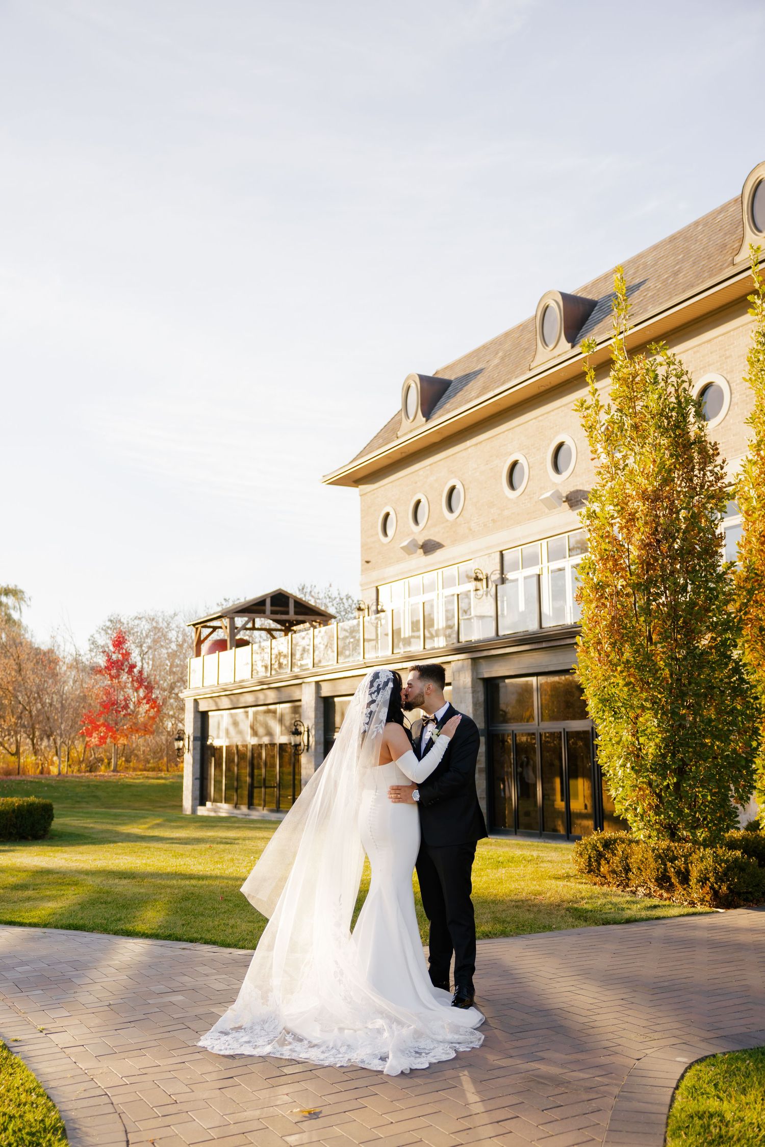 Autumn wedding scene with couple dancing by grand building and golden trees.