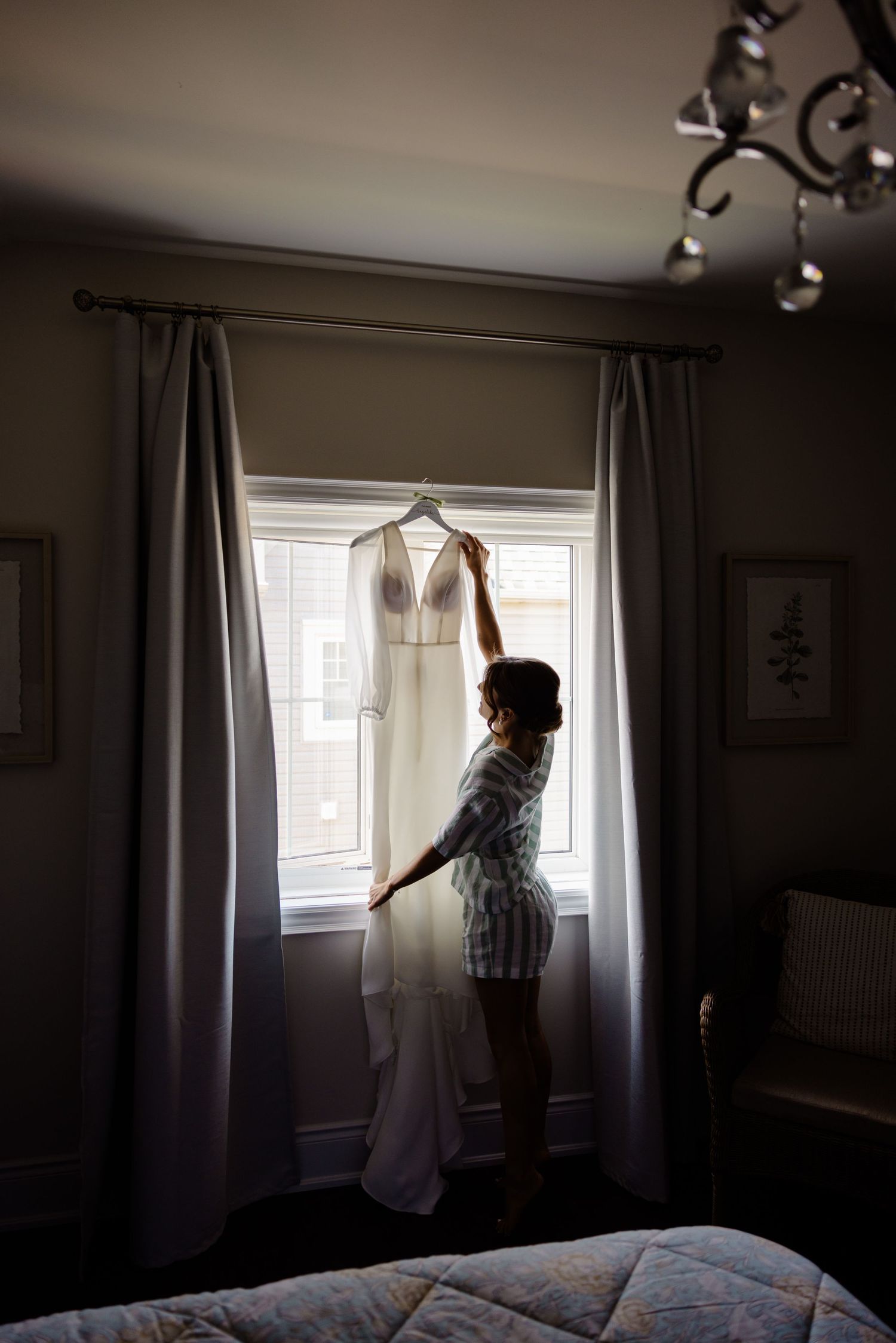 Silhouette of someone adjusting a wedding dress hanging in front of a window.