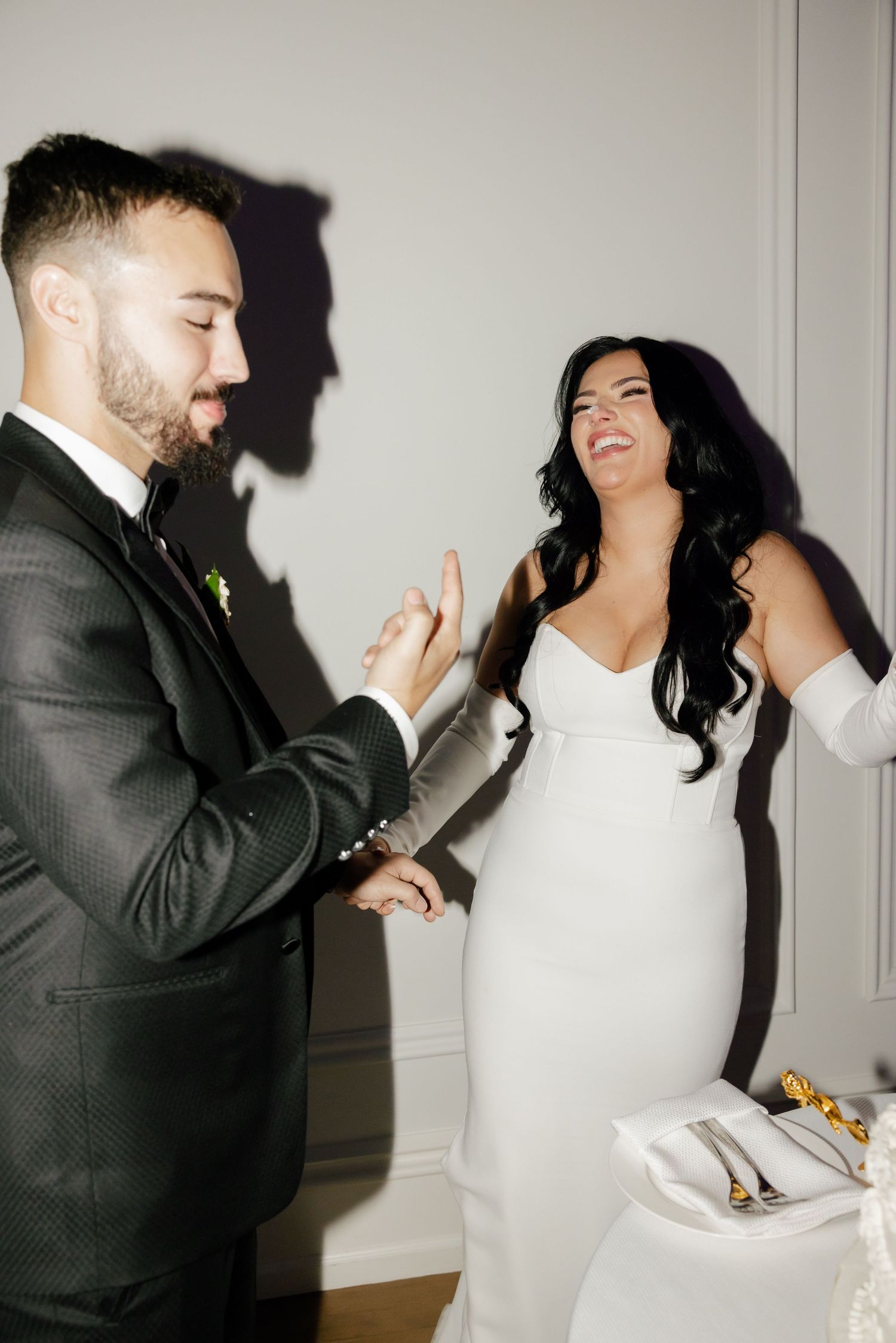 Candid moment of newlyweds laughing while feeding each other wedding cake.
