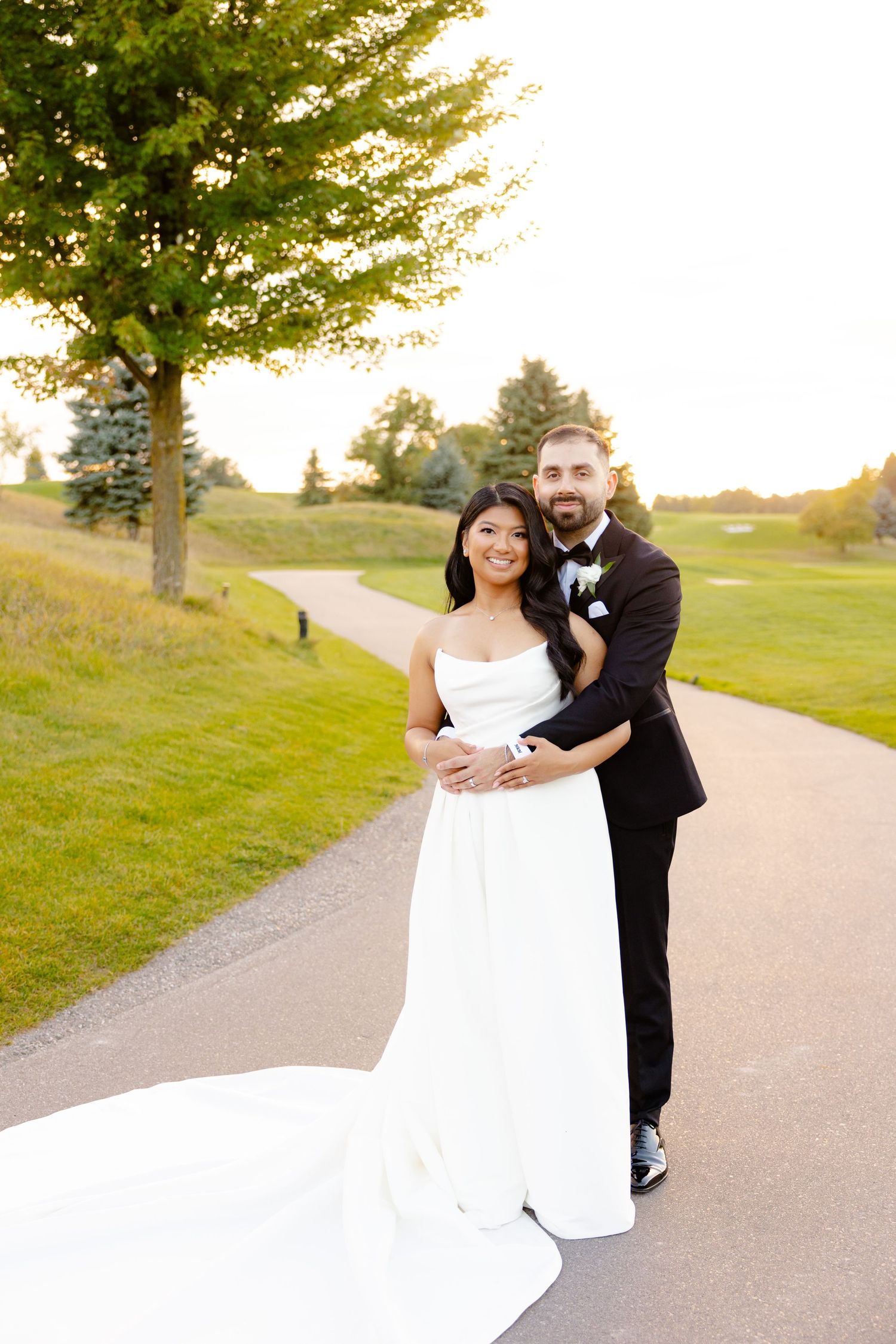 Newlyweds embrace on a path at a golf course during golden hour sunset.