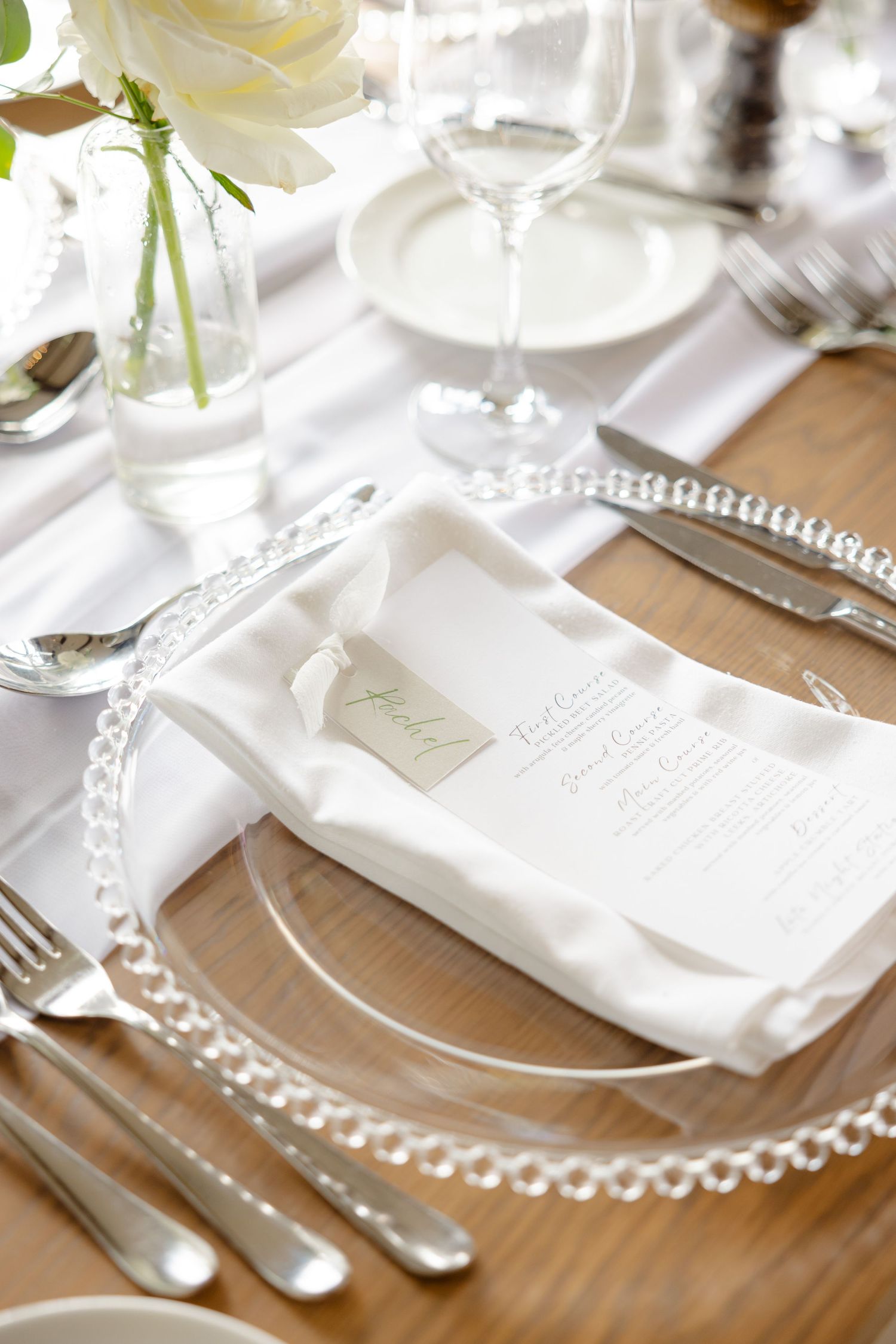 Close-up of elegant wedding table setting with pearl charger plate and white menu card.