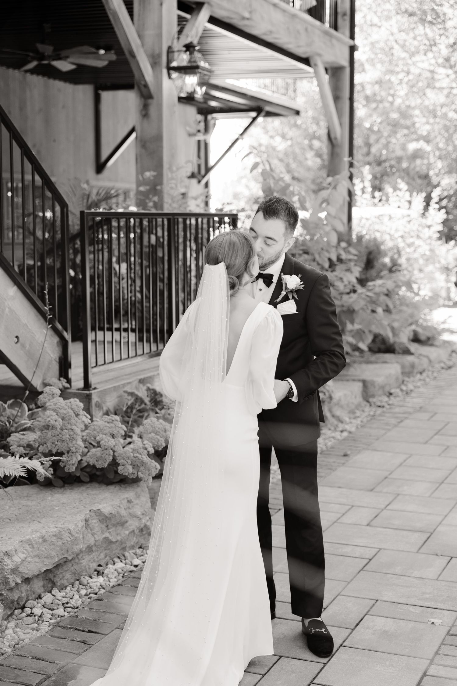 Monochrome wedding photo of couple sharing an intimate moment beneath rustic wooden architecture.