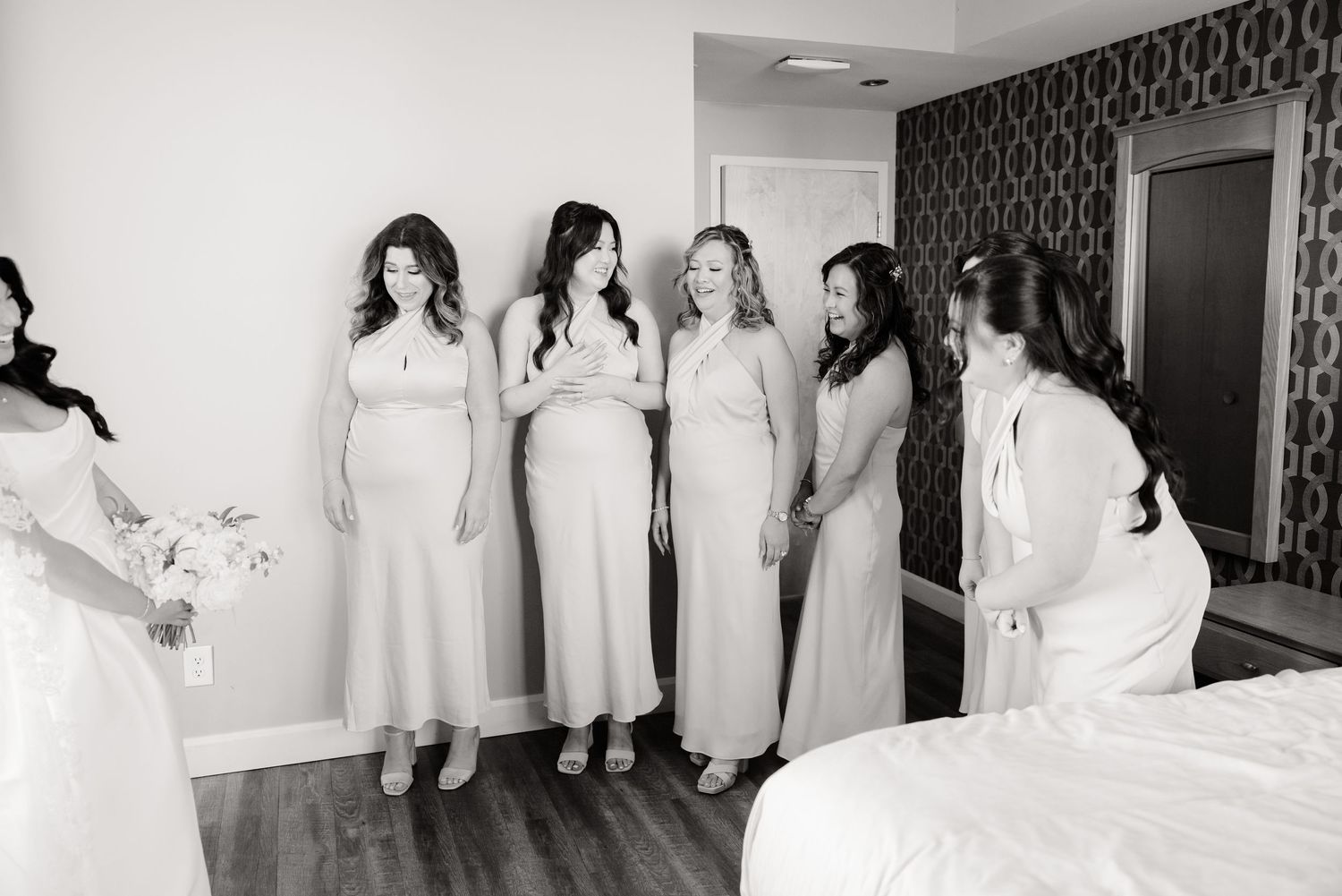 Black and white photo of bride and bridesmaids sharing candid moment in hotel room.
