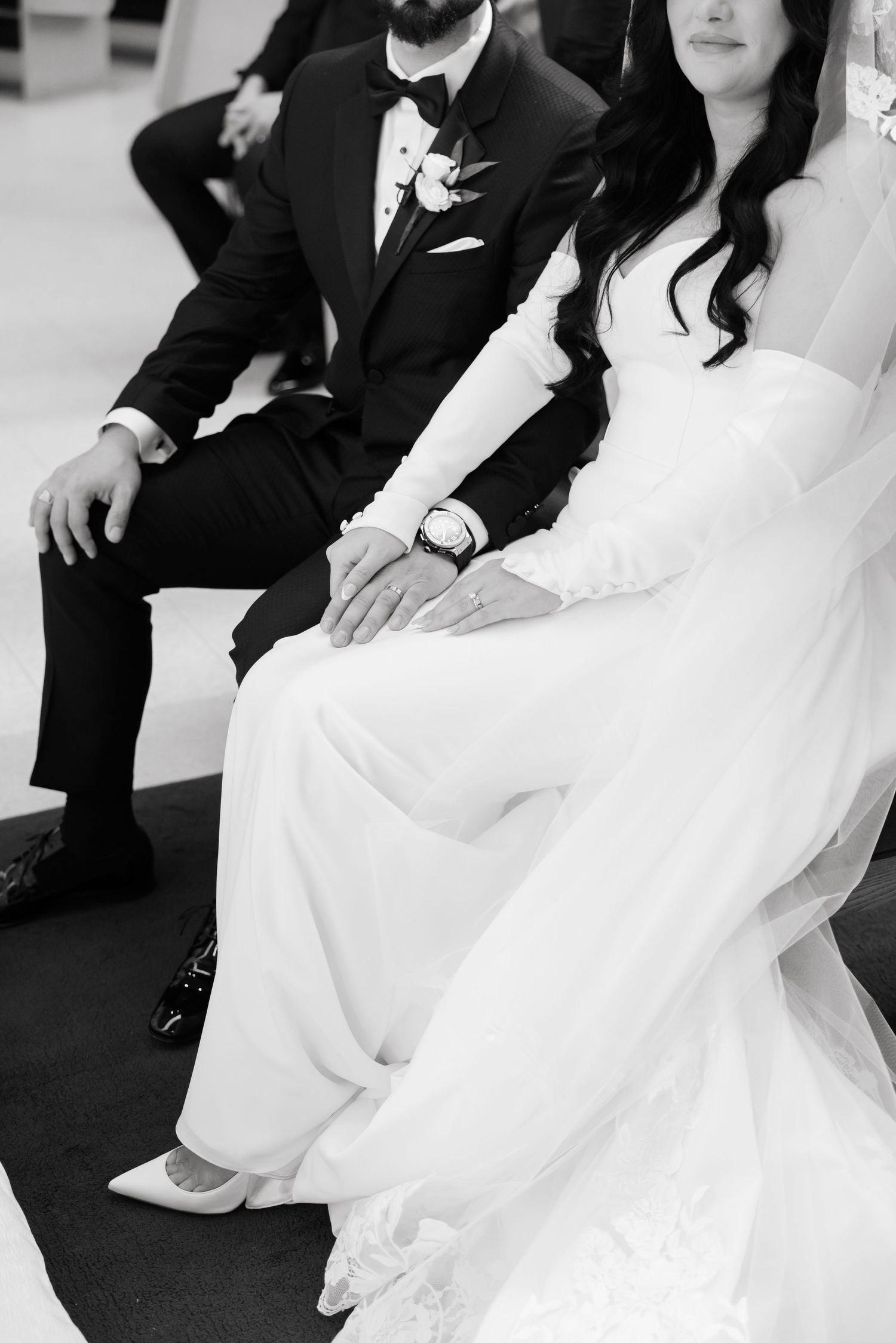 Black and white detail shot of newlyweds sitting together showing formal attire.