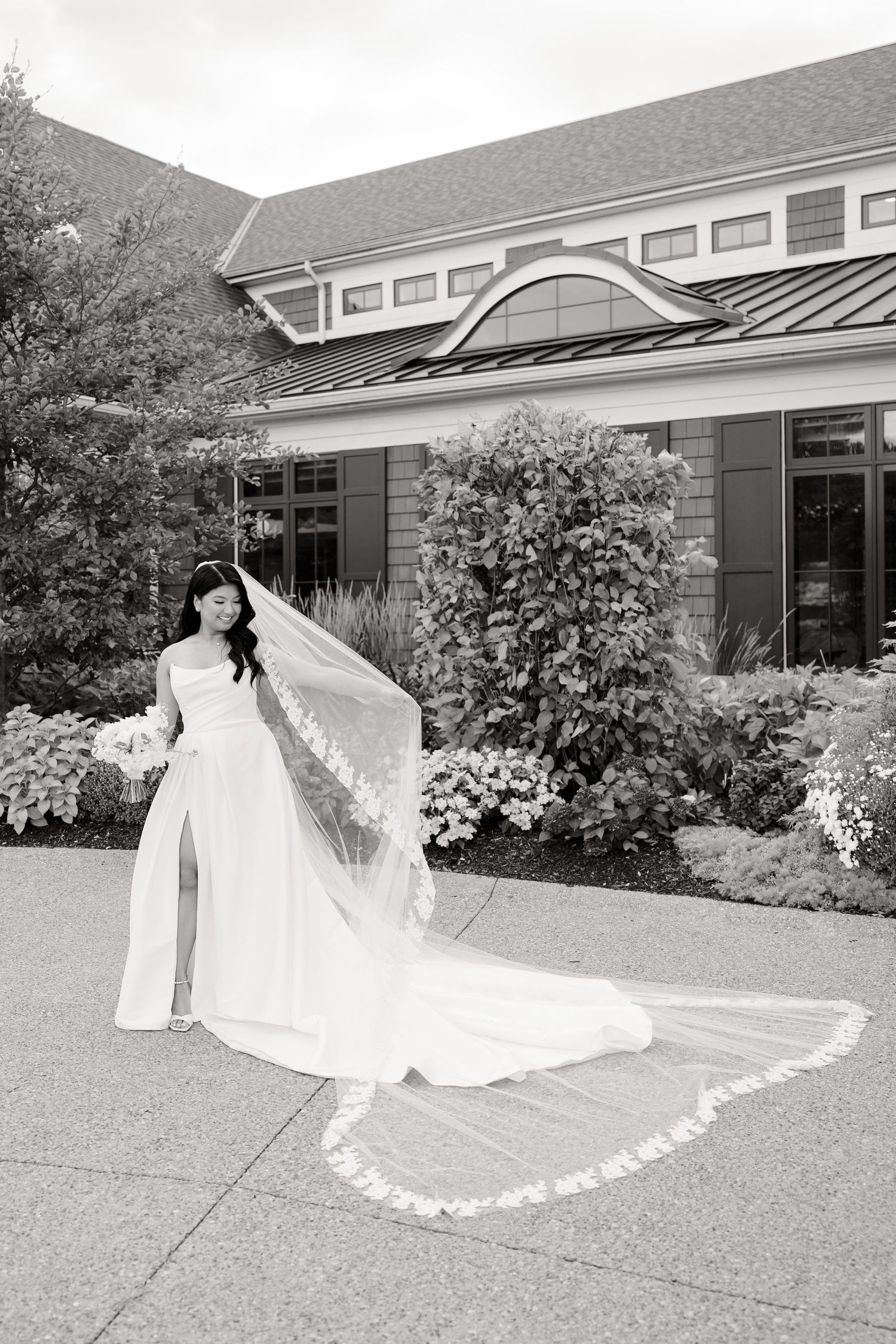 Black and white wedding photo highlighting elegant bridal gown and veil against architectural backdrop.