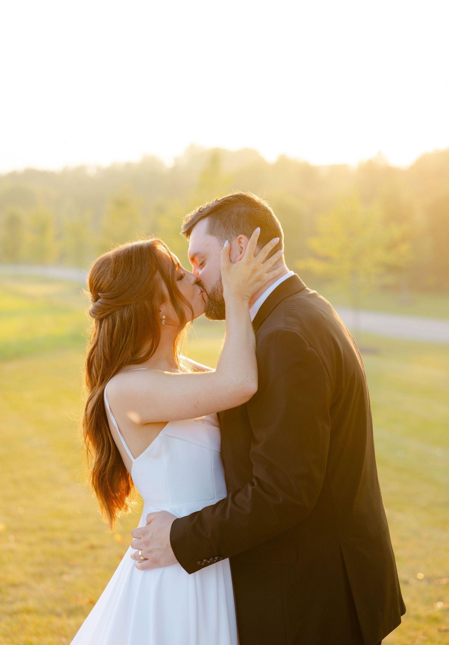 Intimate wedding moment captured during golden hour with couple embracing against sunlit background.