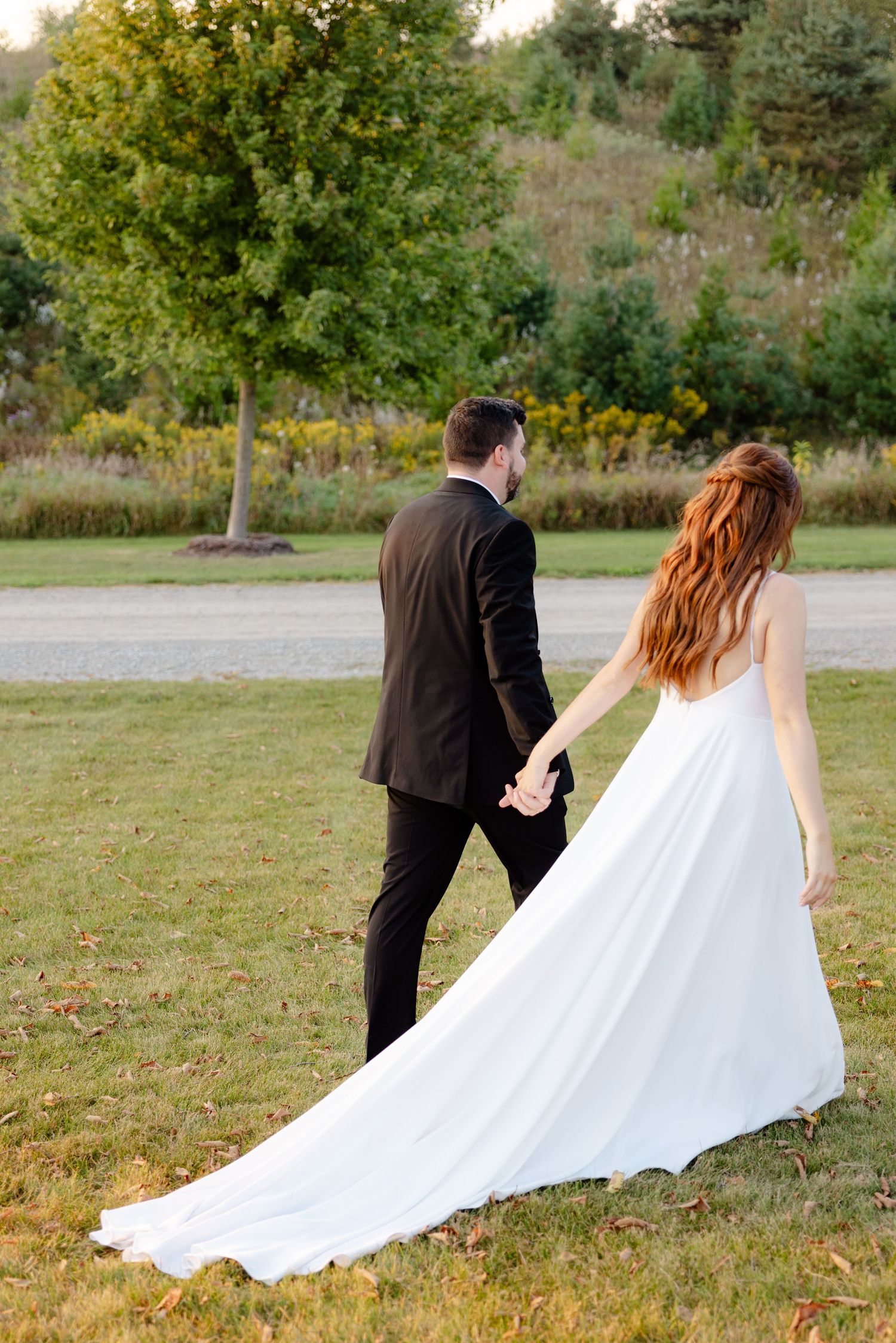 Newlywed couple walking through garden path with flowing white wedding dress train.