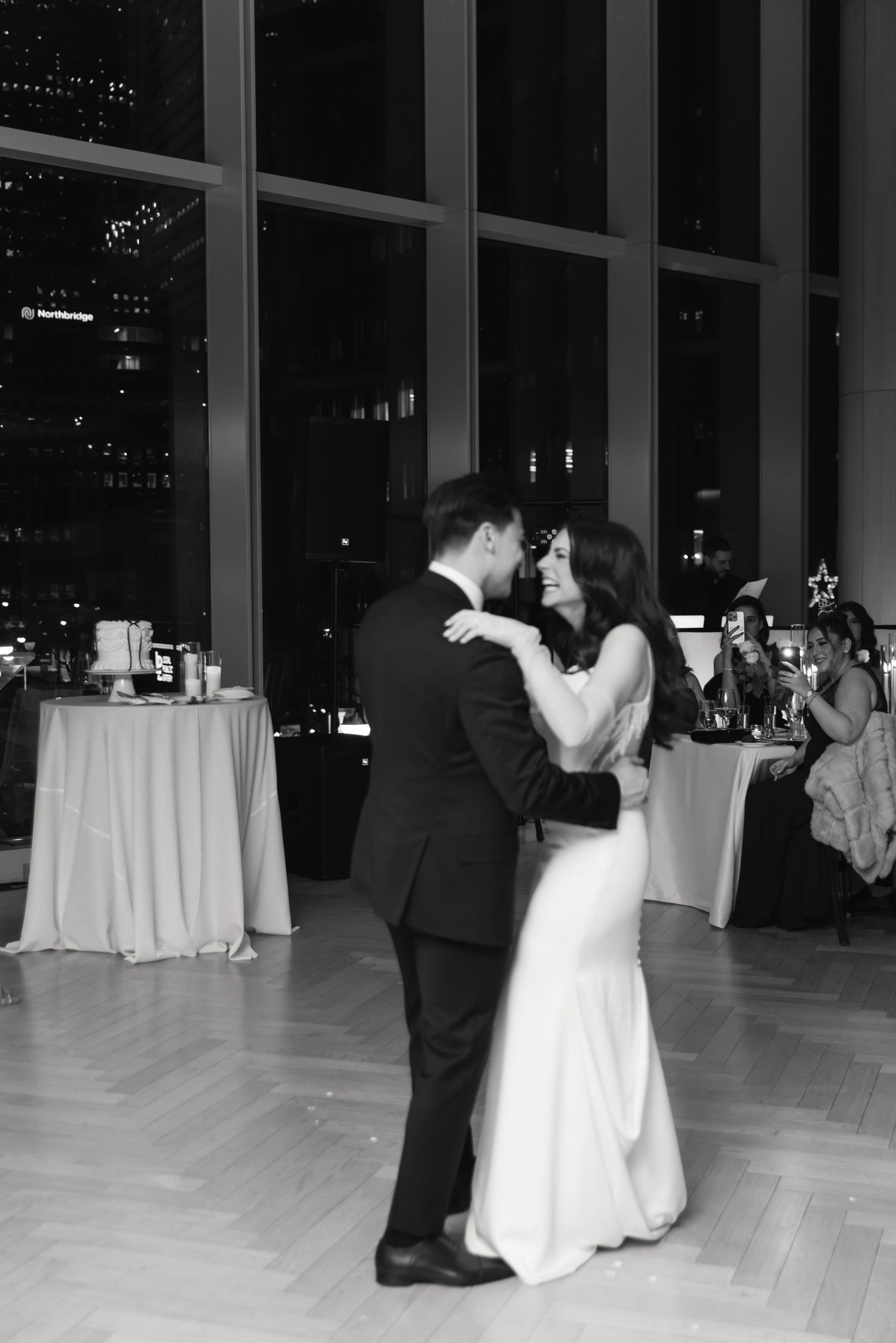 Black and white reception photo of couple's romantic dance beneath crystal chandeliers.
