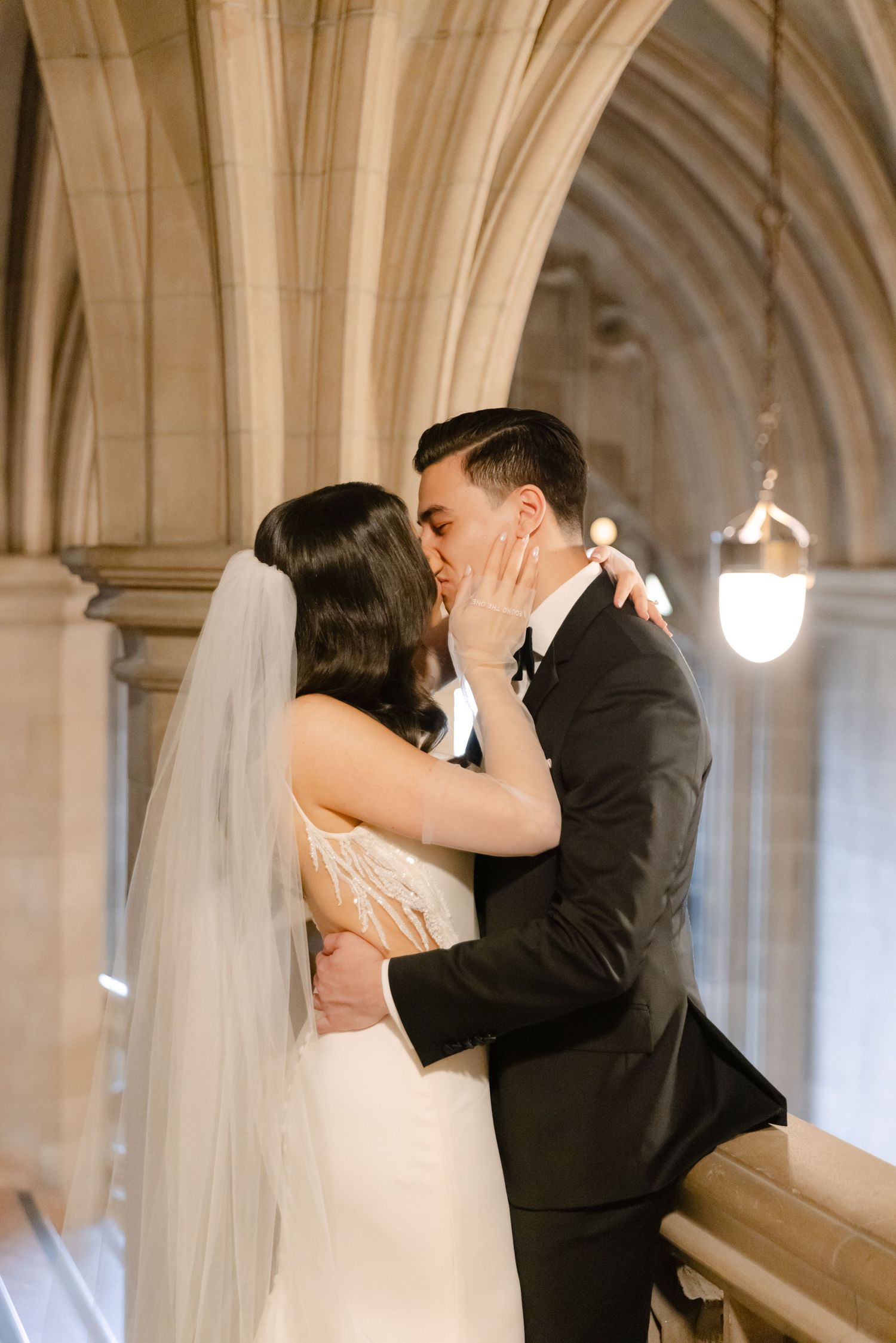 Tender wedding moment captured in elegant stone corridor with vintage lighting.