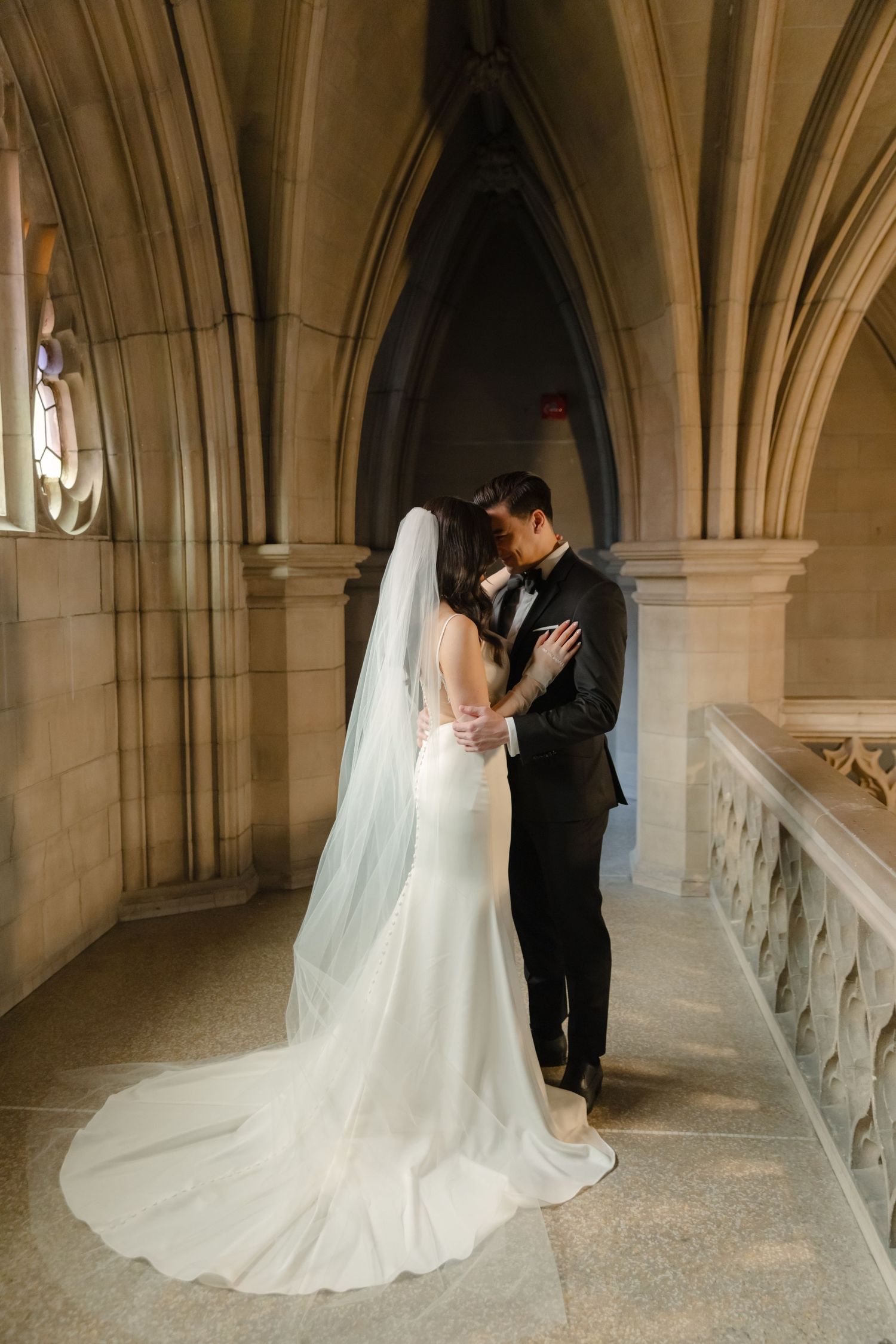 A romantic wedding portrait with flowing veil against gothic stone architecture and arched ceilings.