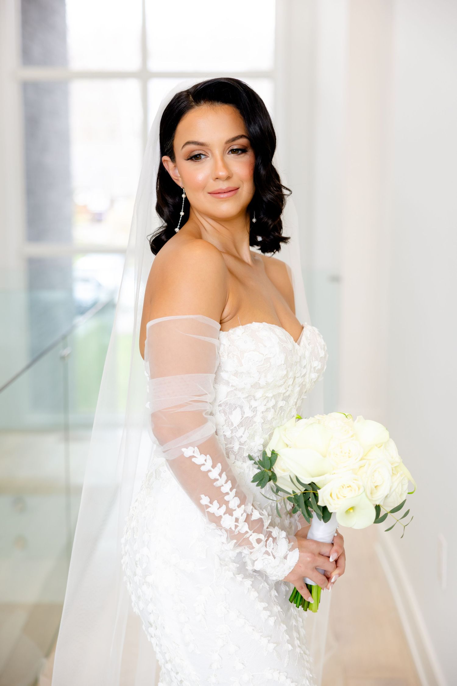 Radiant bridal portrait showcasing intricate lace details and sheer sleeves with white floral bouquet.