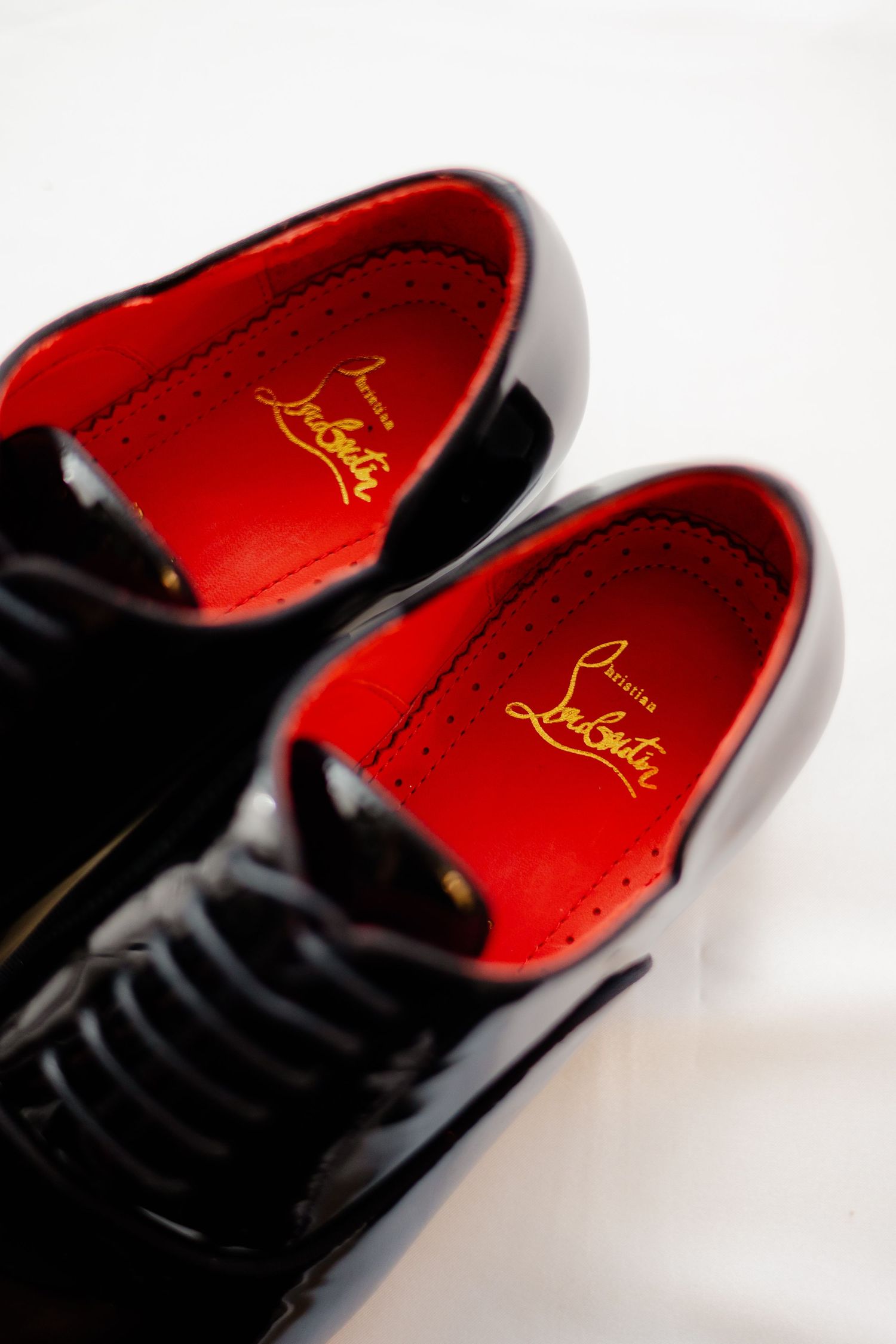 Close-up of black patent leather dress shoes with red soles and gold branding.