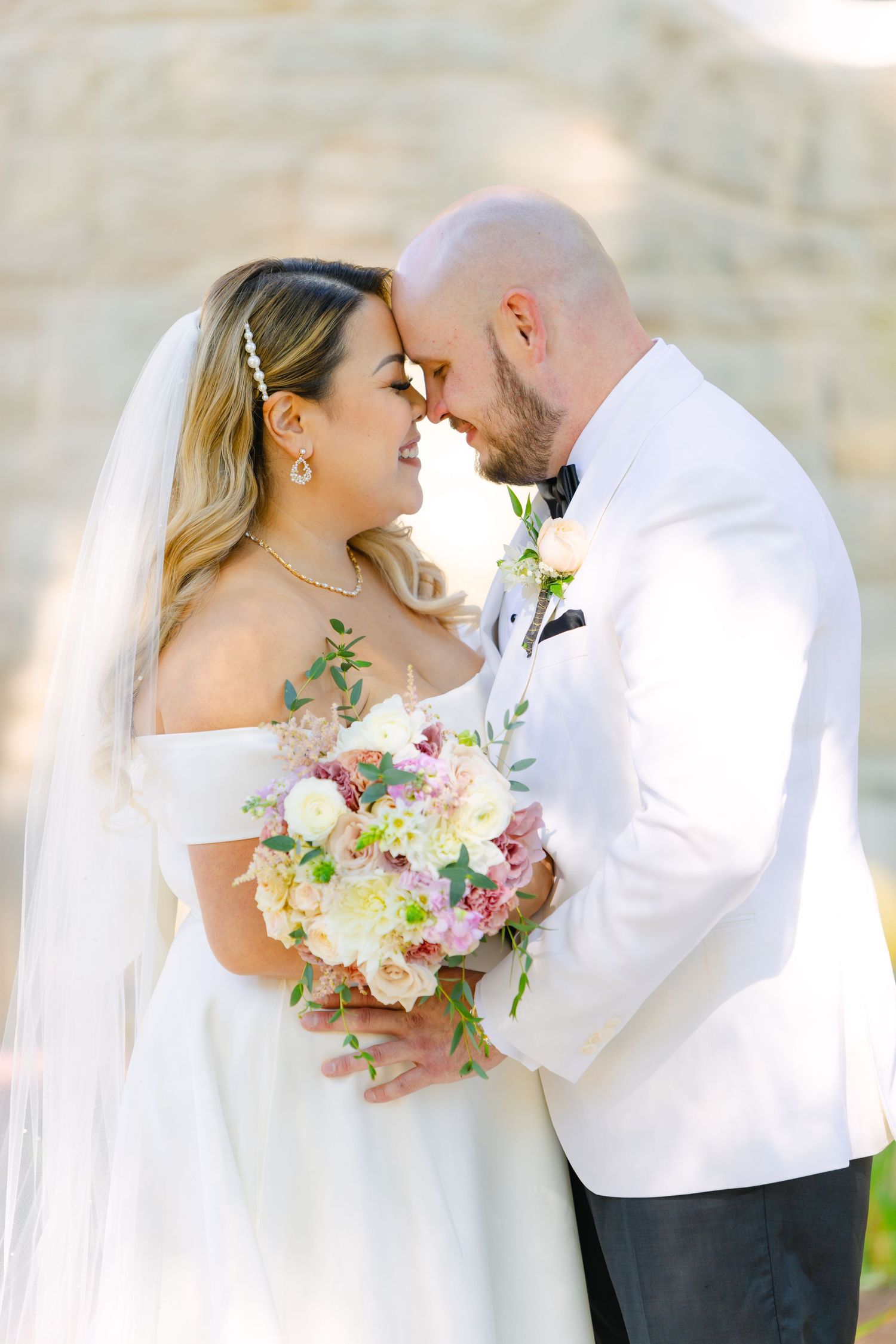 Romantic wedding portrait of couple sharing intimate moment with pastel floral bouquet.