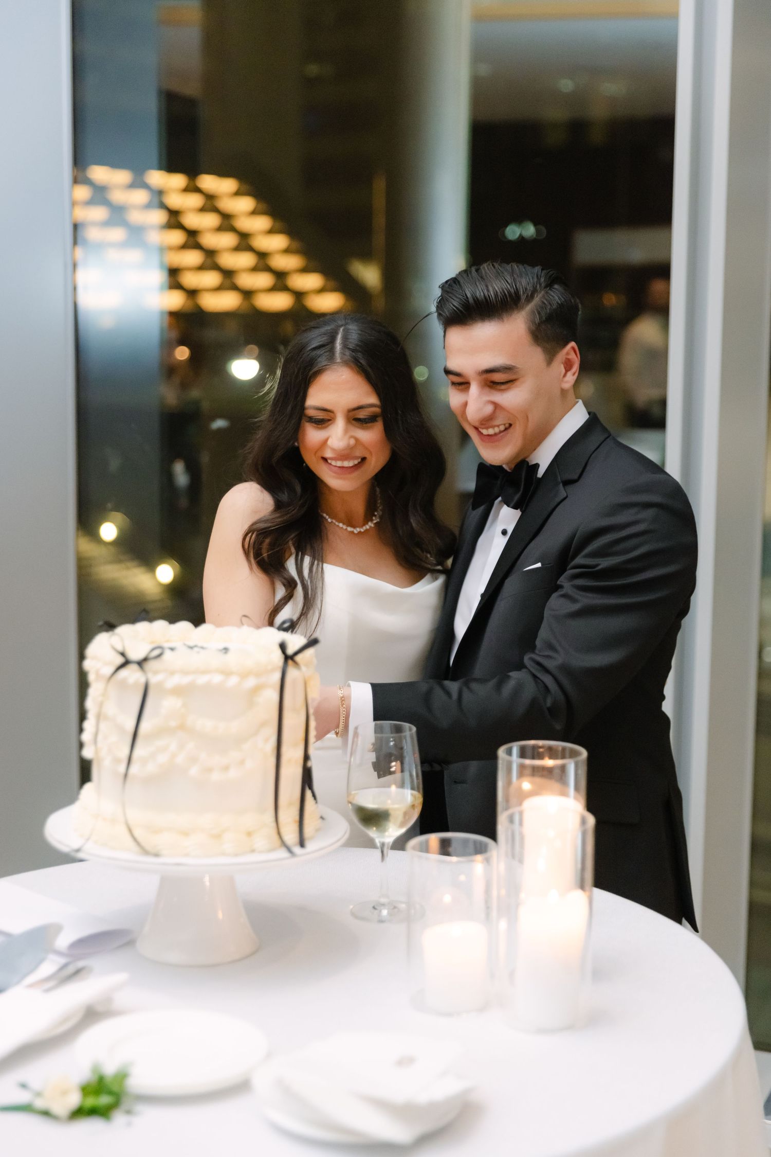 Bride and groom laughing together while cutting their elegant white wedding cake.