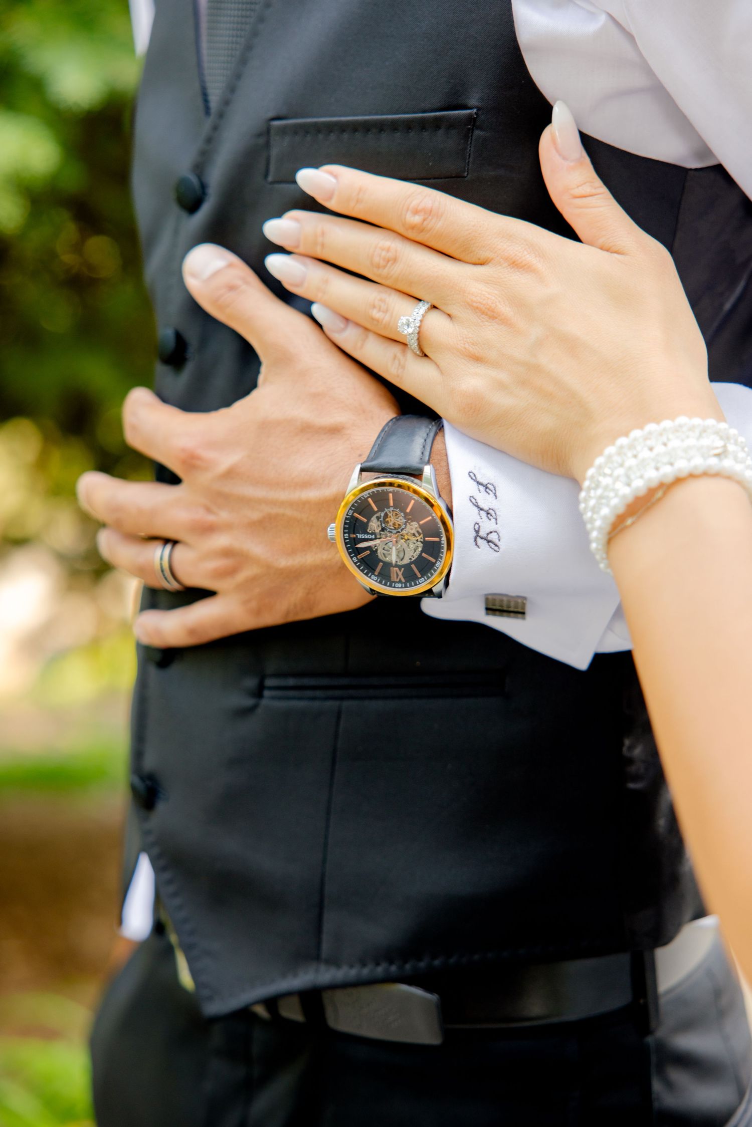 Close-up of wedding rings and watch detail as hands embrace.