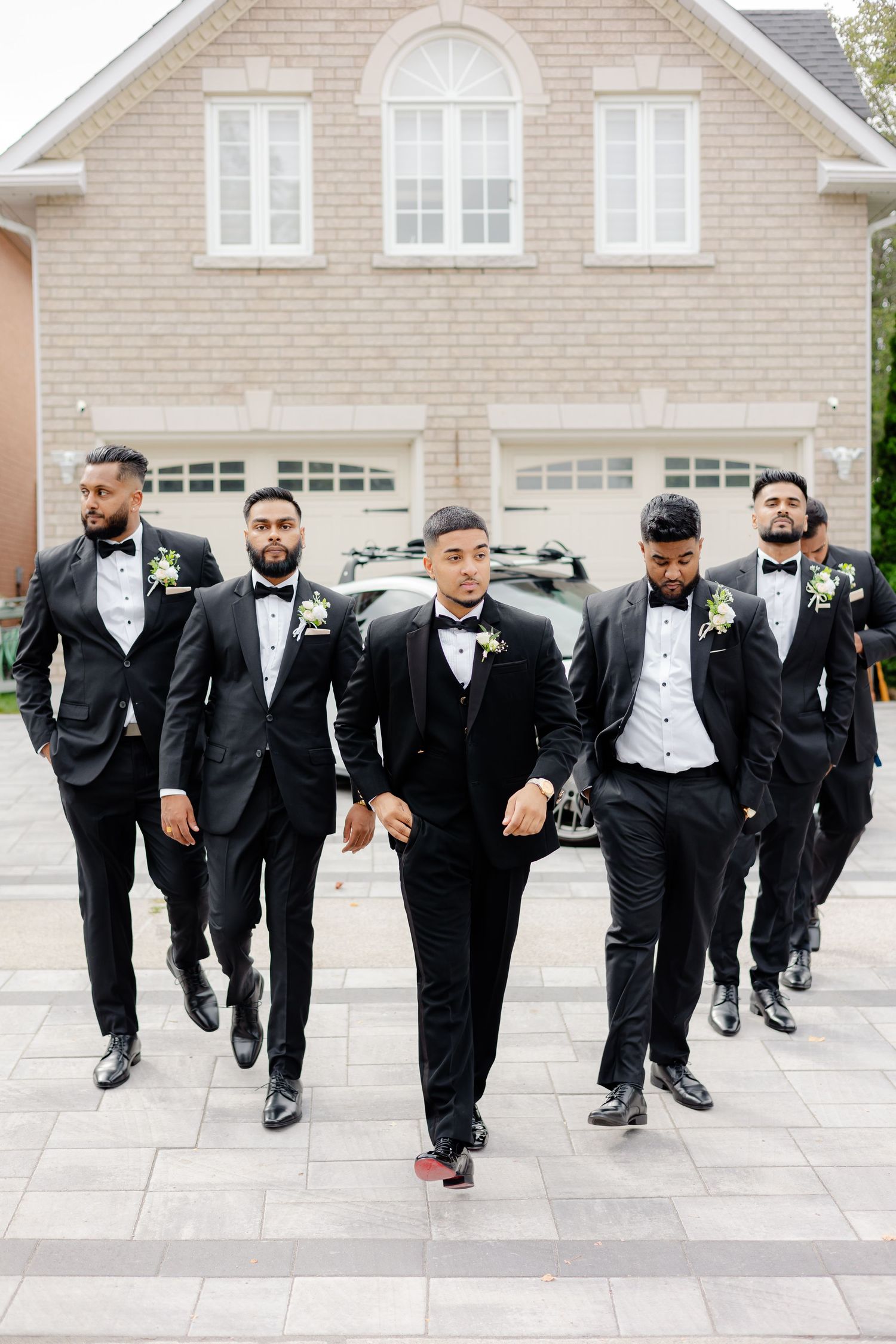 Groomsmen walking in formation wearing matching black tuxedos and bow ties.