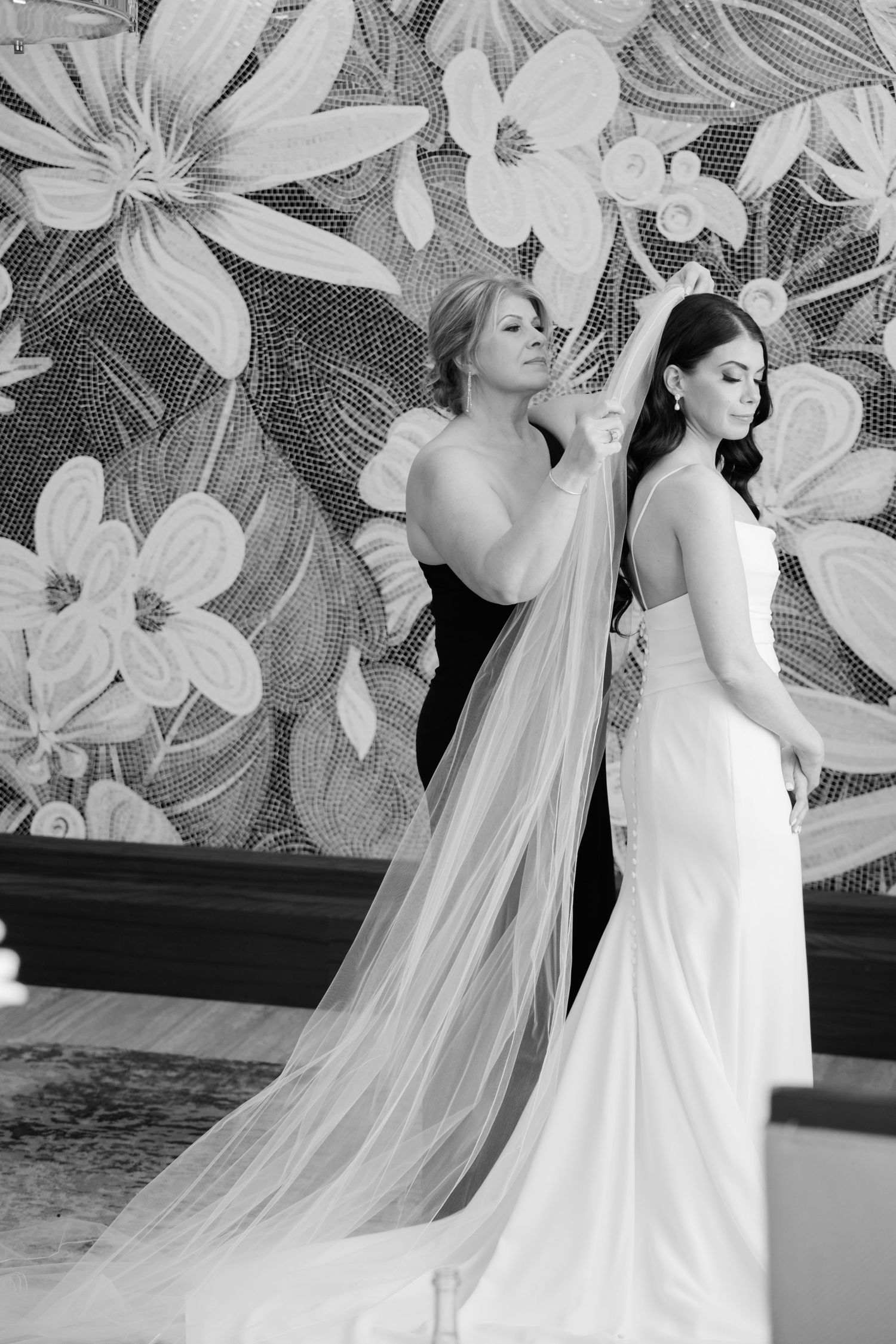 Black and white wedding photo with dramatic floral backdrop and flowing veil.