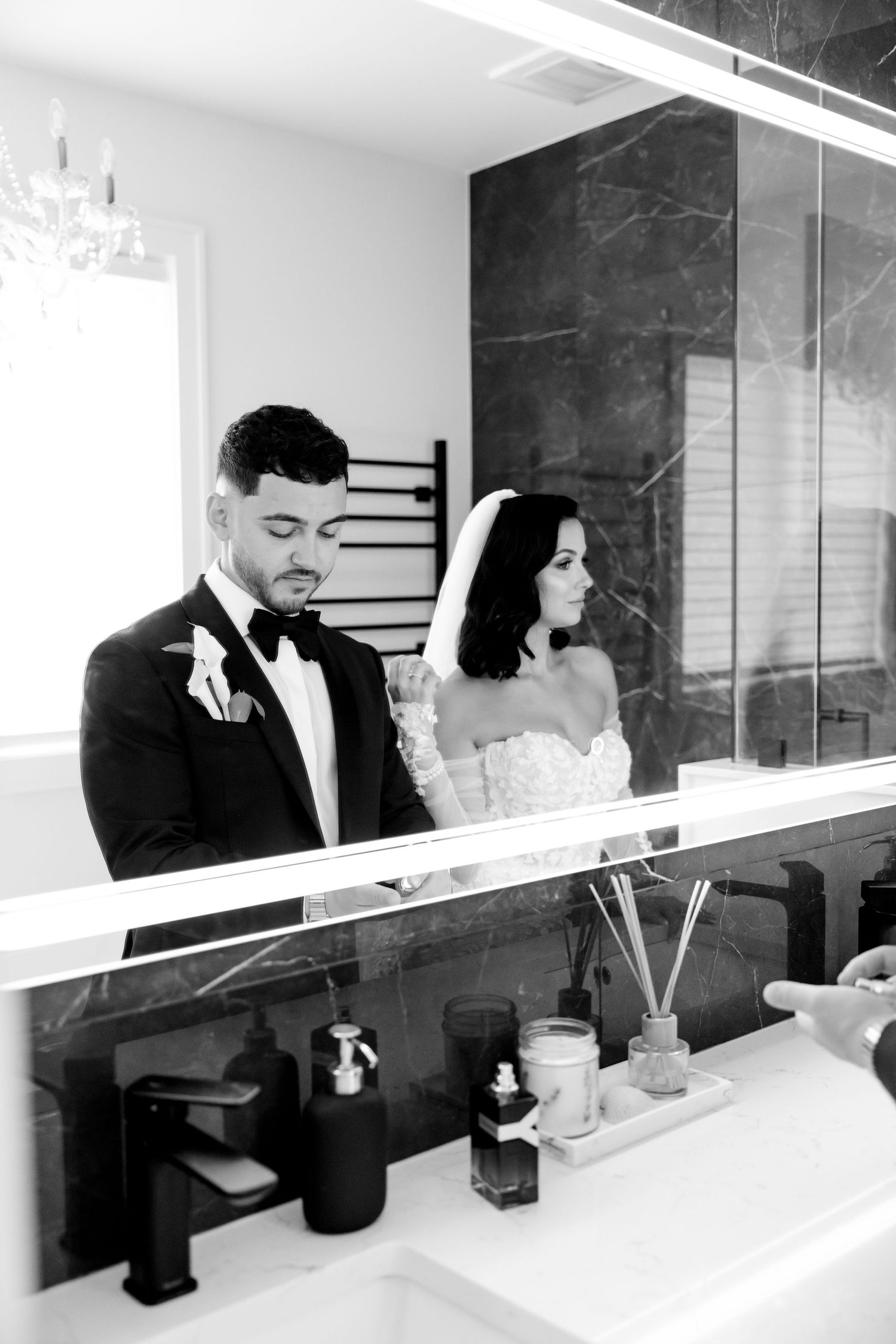 A wedding couple reflected in a modern bathroom mirror with black marble wall accents.