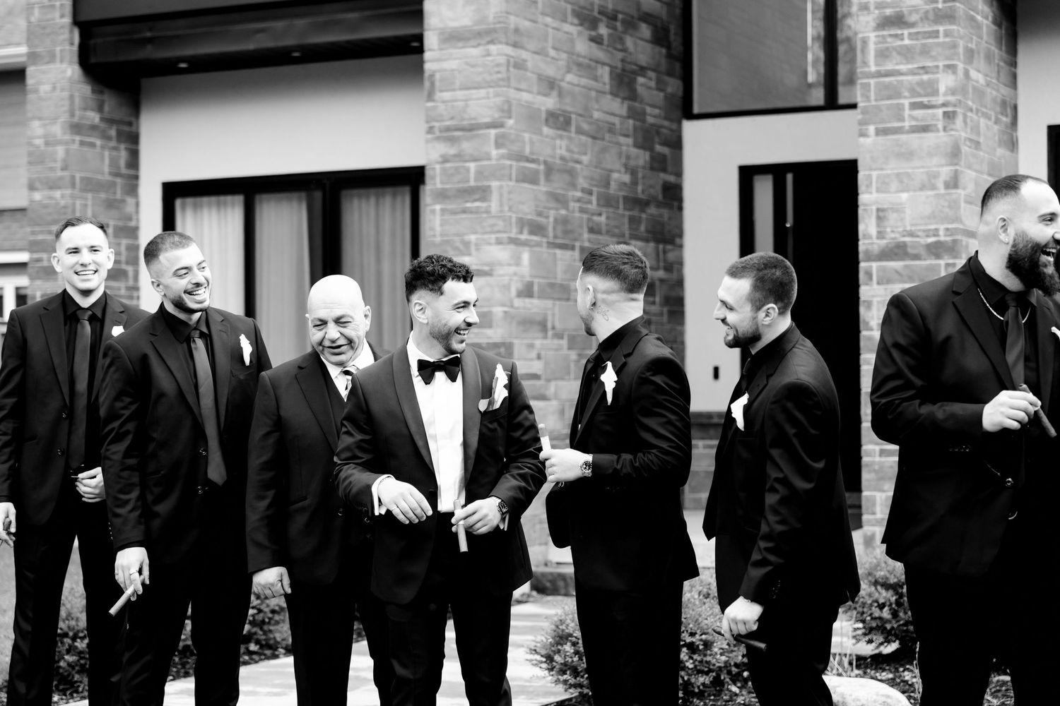 Black and white photo of groomsmen gathered outside a brick building.