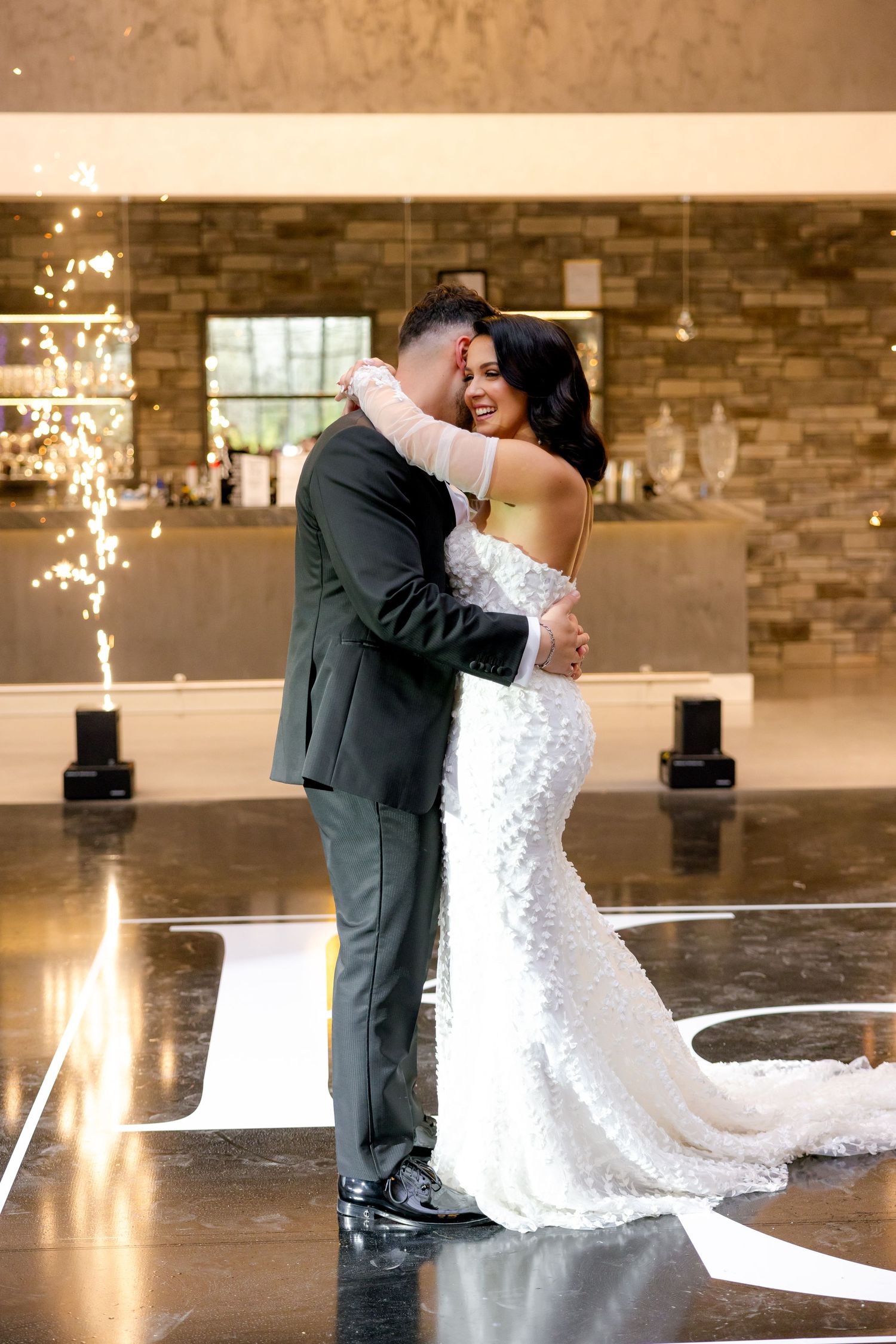 Newlyweds share their first dance surrounded by sparklers in an elegant venue with stone walls and polished floors.