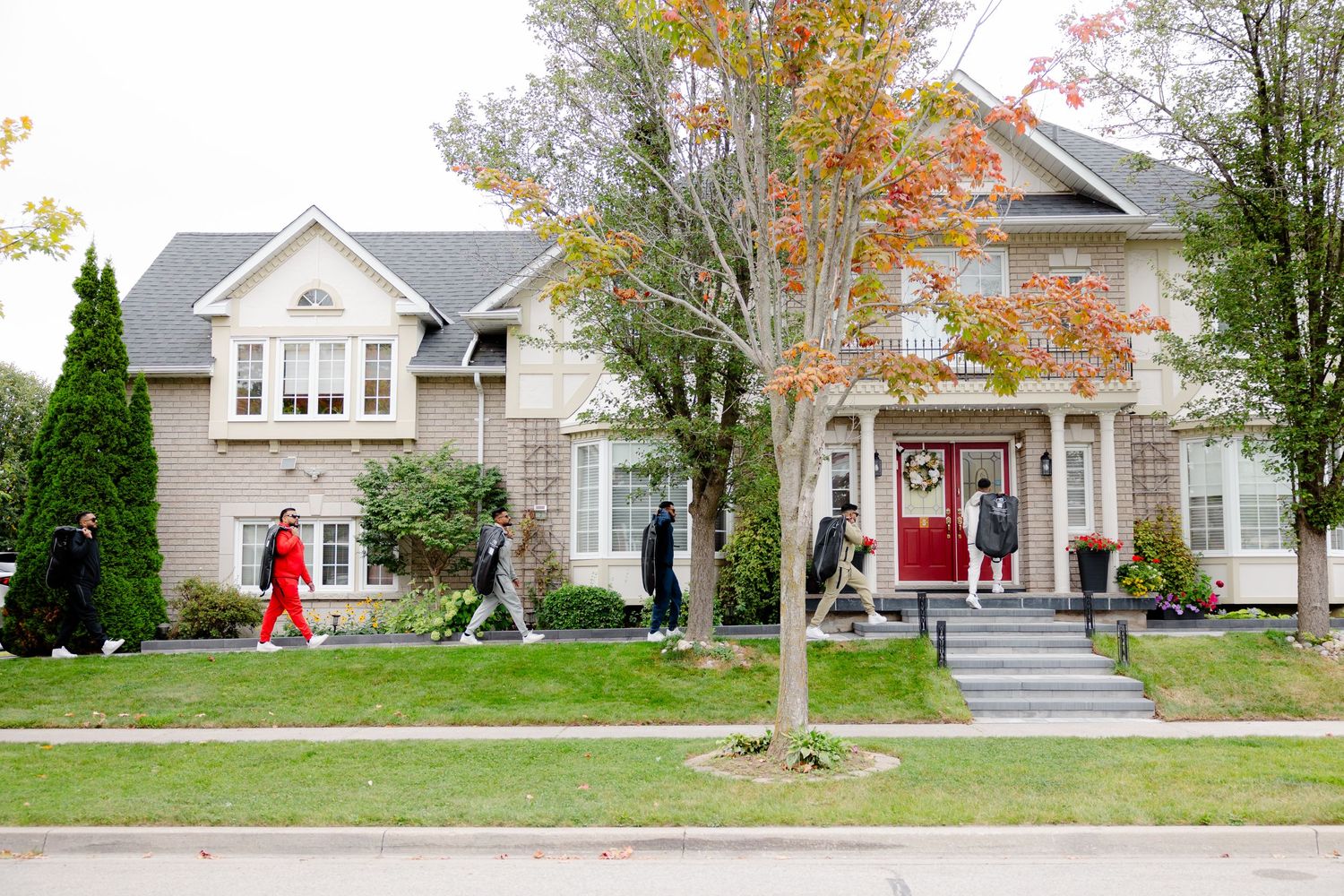 People walking between two elegant suburban homes with red doors and manicured lawns.
