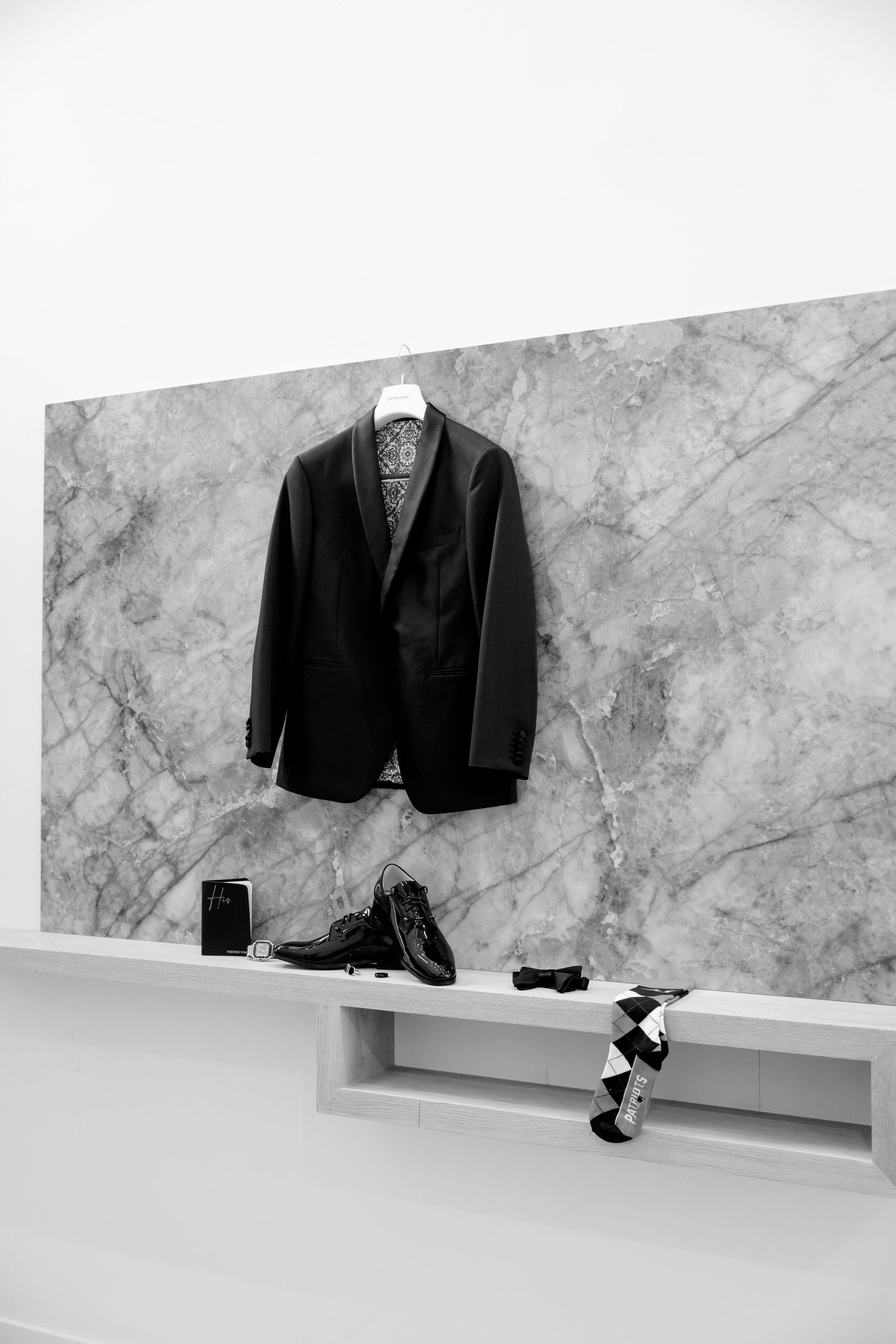 A black suit jacket and dress shoes displayed against a marble wall.